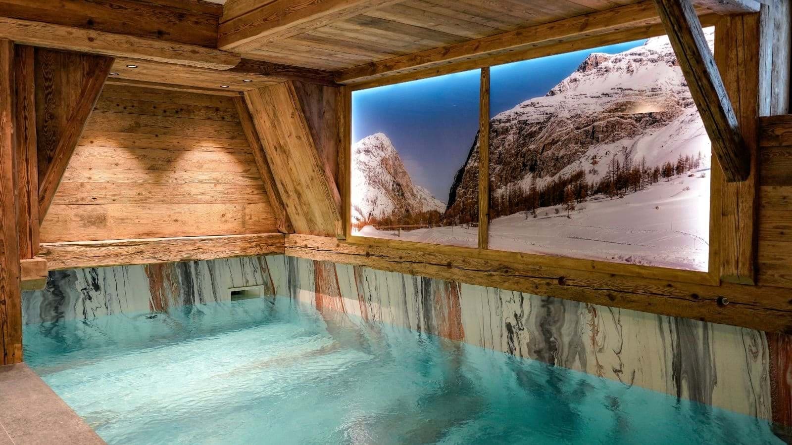 Indoor heated pool with marble lining and backlit mountain mural