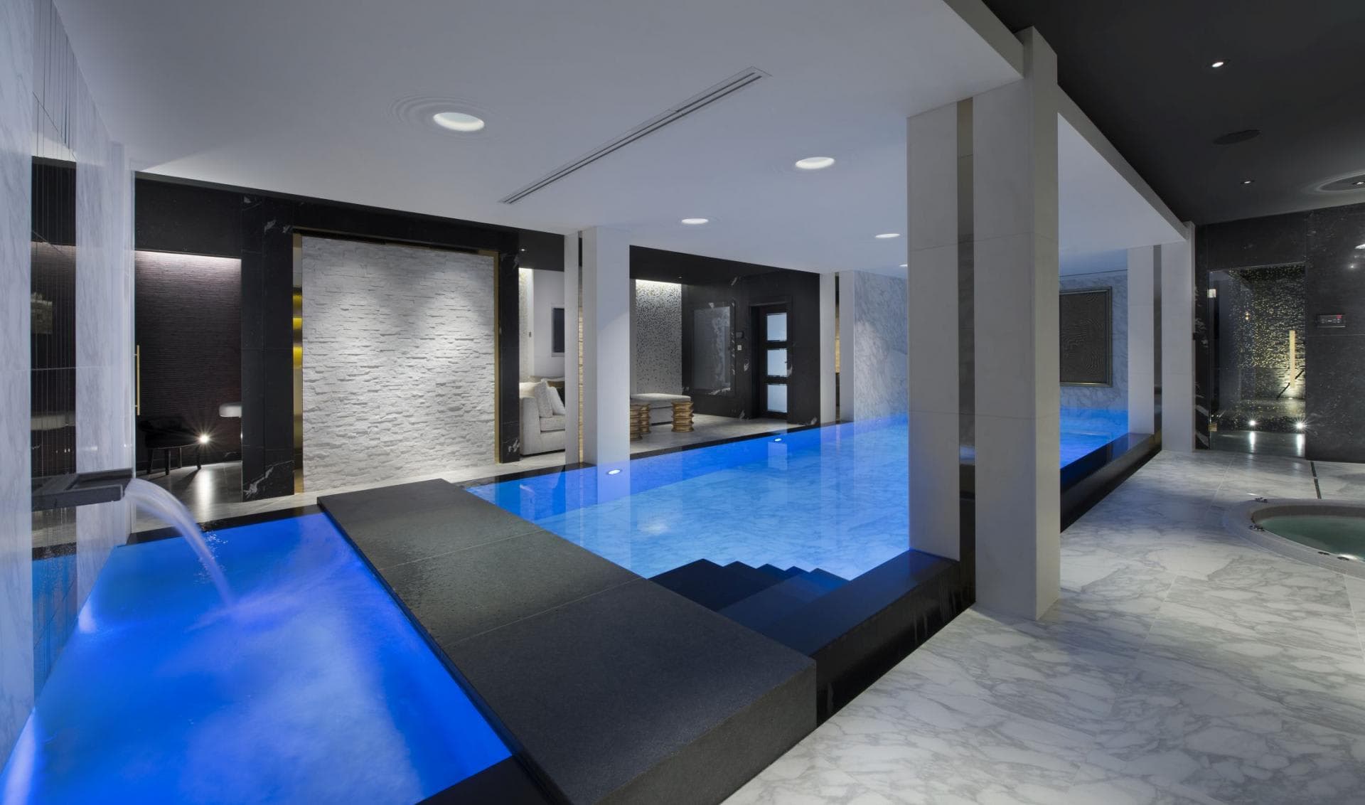 Indoor pool area with waterfall feature and adjacent hot tub