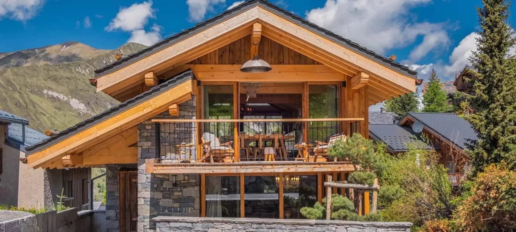 Timber and stone chalet facade with mountain-view balcony seating