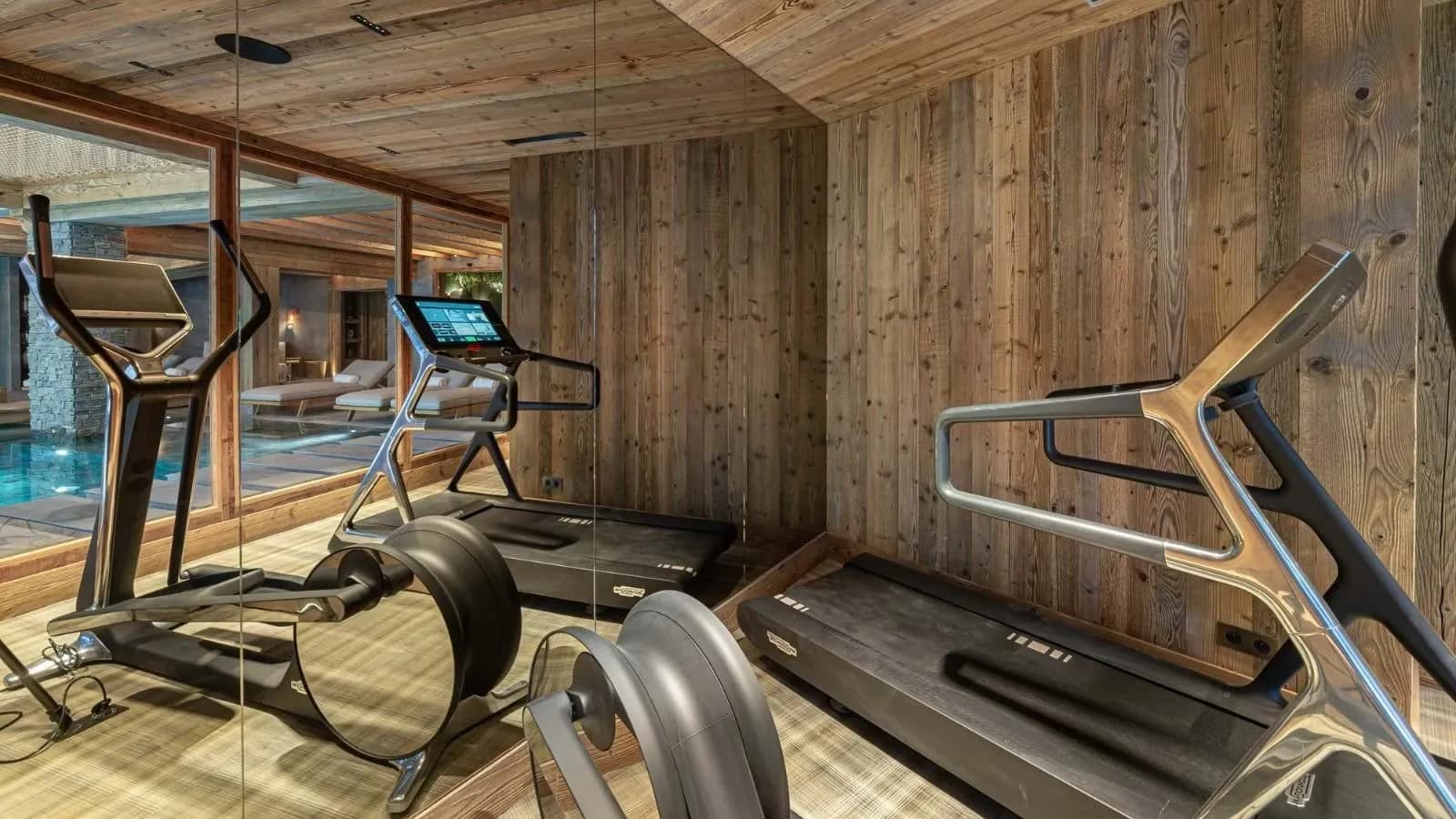 Fitness room with a treadmill and rowing machine beside the indoor pool