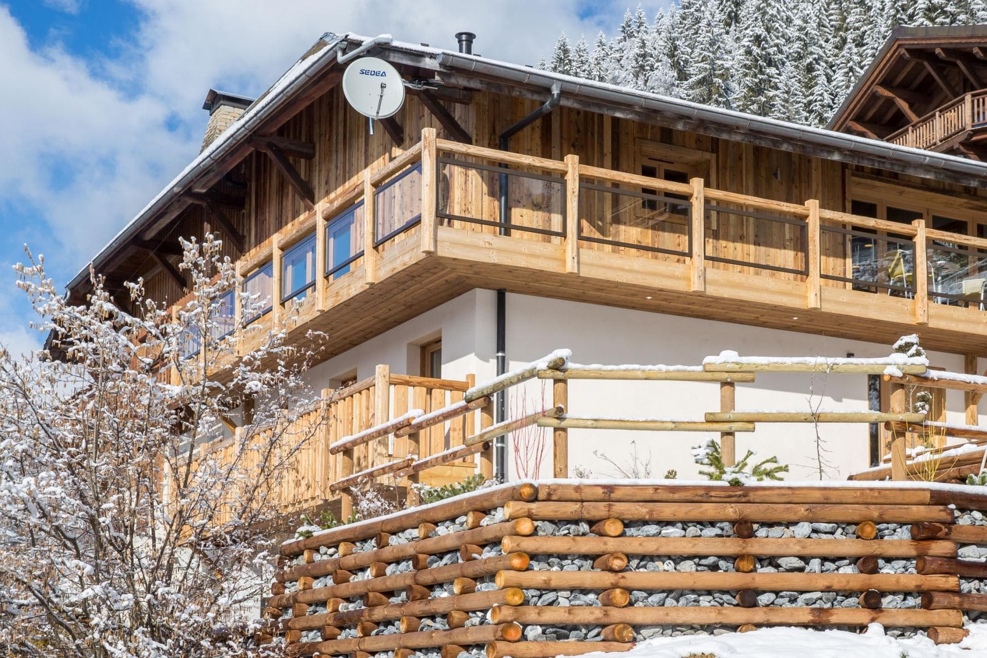 Timber chalet featuring glass-paneled wrap-around balcony and snowy mountain backdrop
