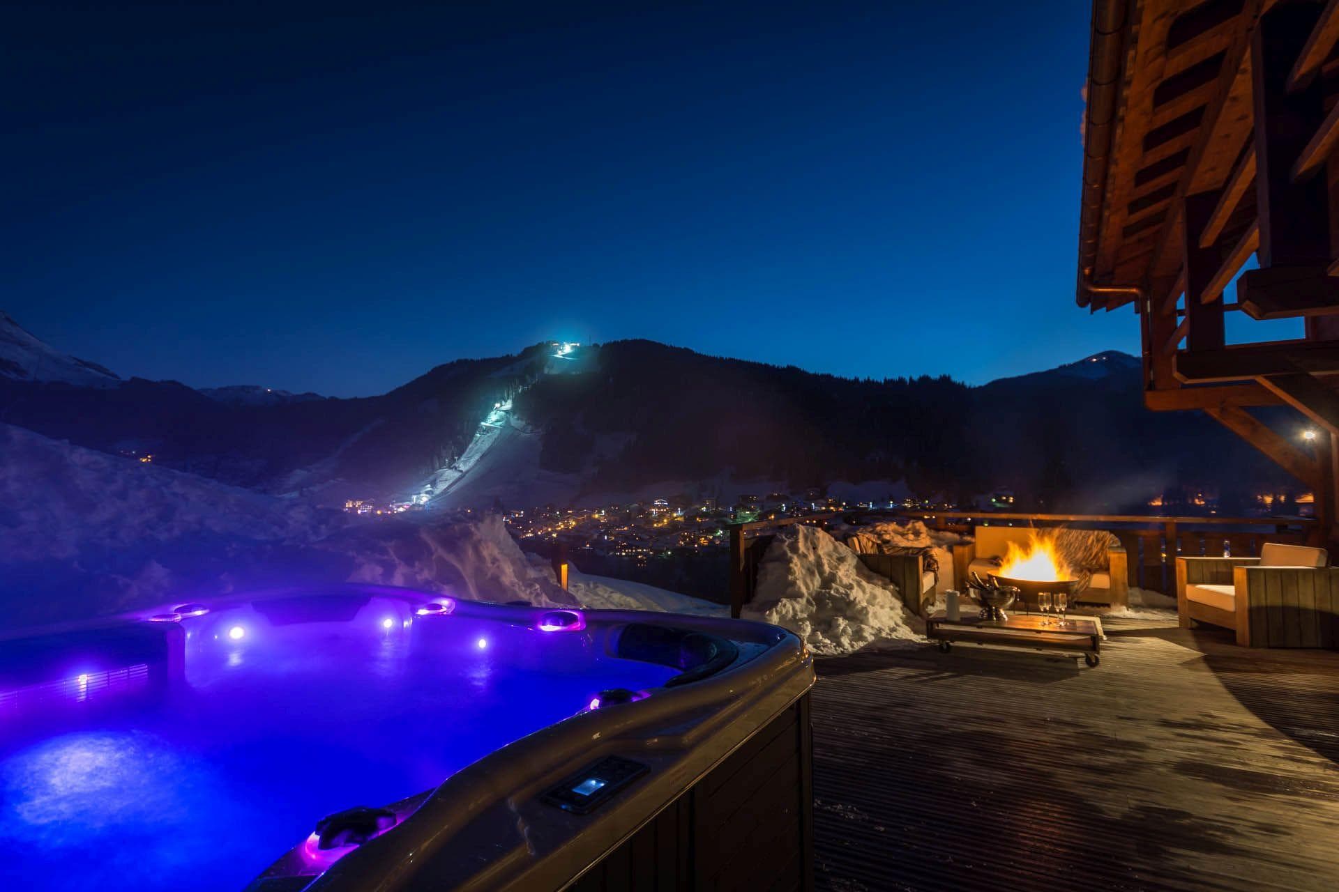 Heated terrace with hot tub, fire pit, and illuminated ski run views