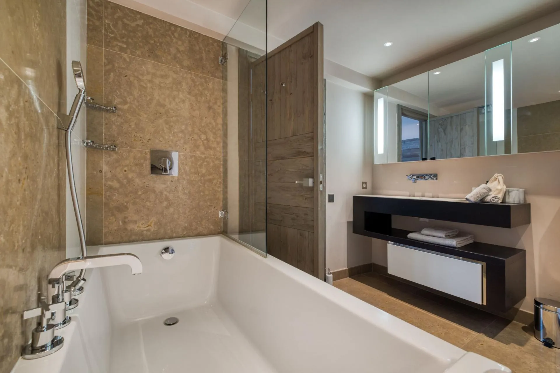 Bathroom with soaking tub, hand-held shower head, and backlit vanity mirror