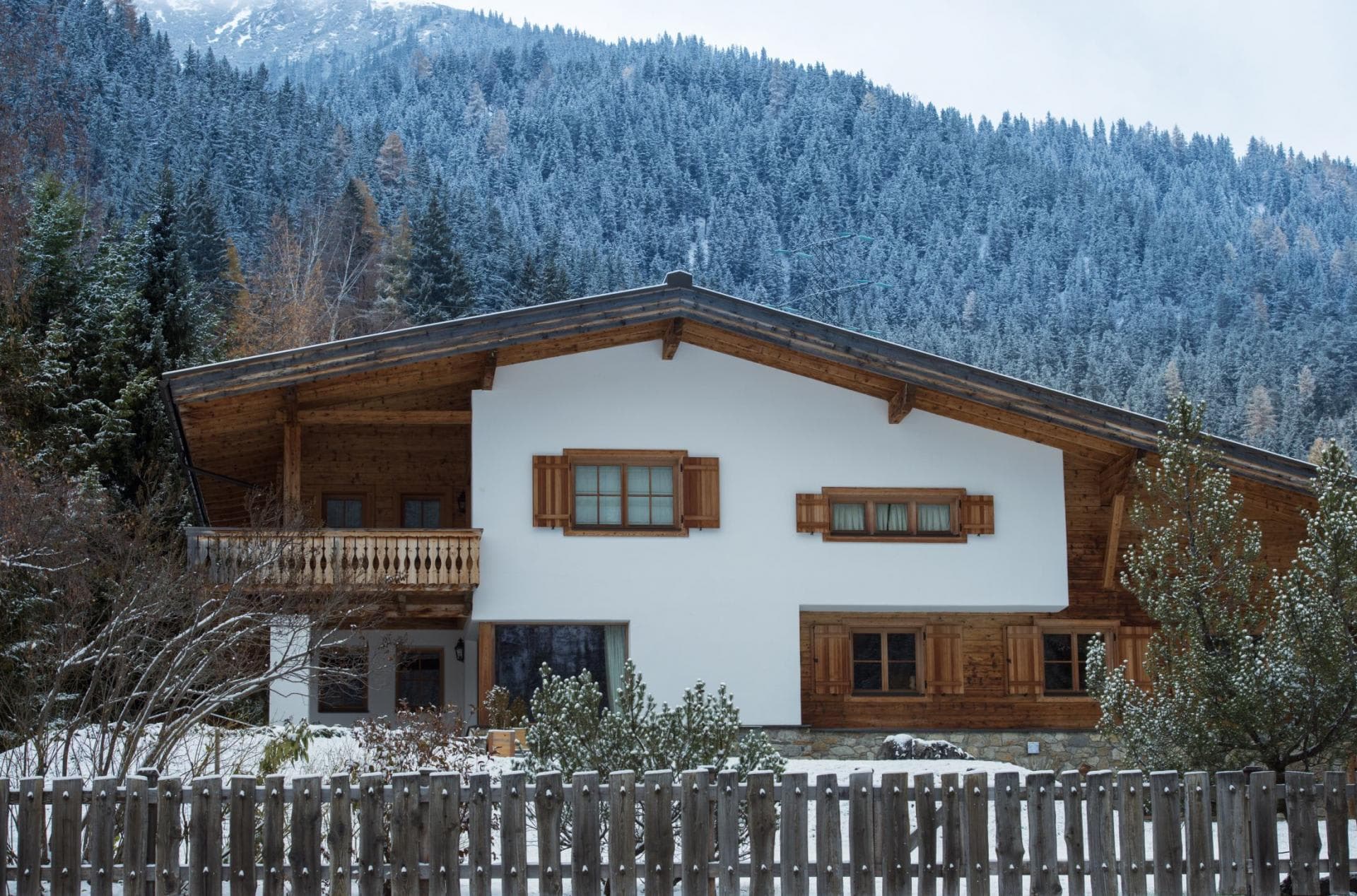 Chalet exterior with private balcony and timber shutters; mountain forest backdrop