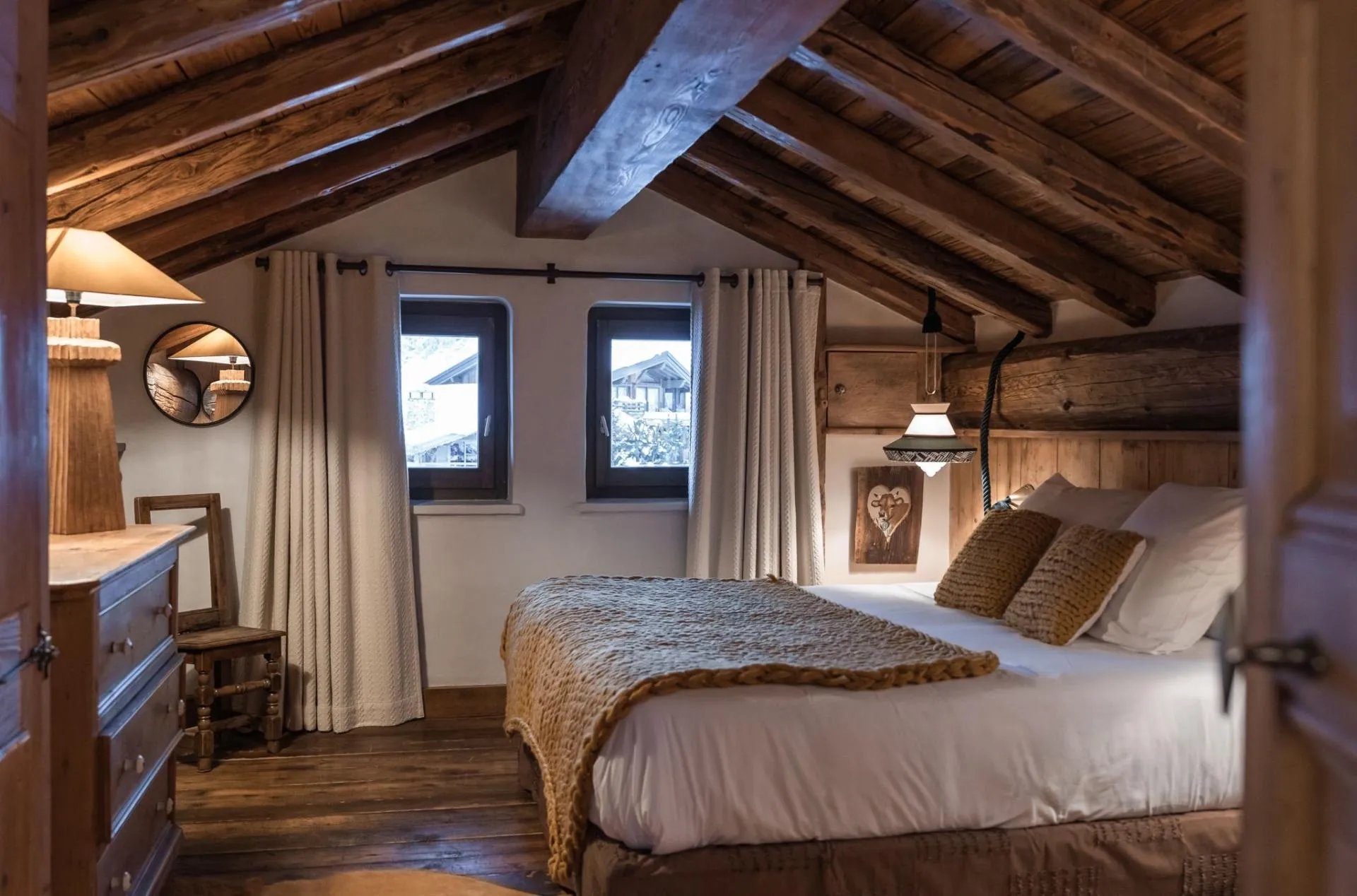 Double bedroom beneath roof beams with windows and seating