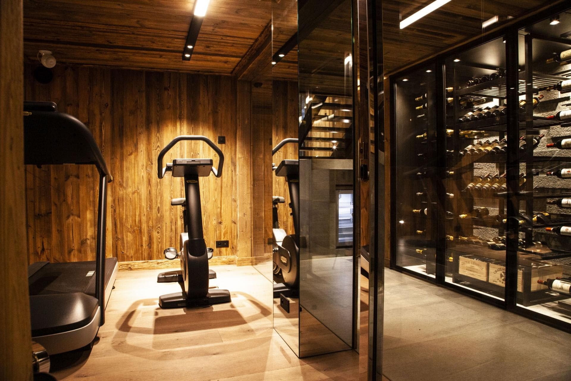 Fitness area with treadmill and exercise bike adjacent to glass-enclosed wine cellar