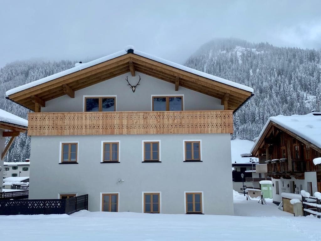 Chalet exterior with upper-level balcony and mountain forest backdrop