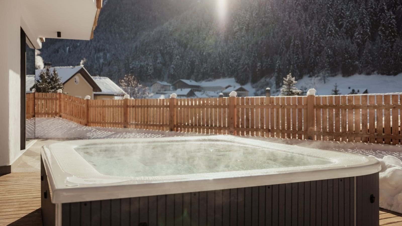 Outdoor hot tub on deck overlooking snow-covered valley and forested mountains