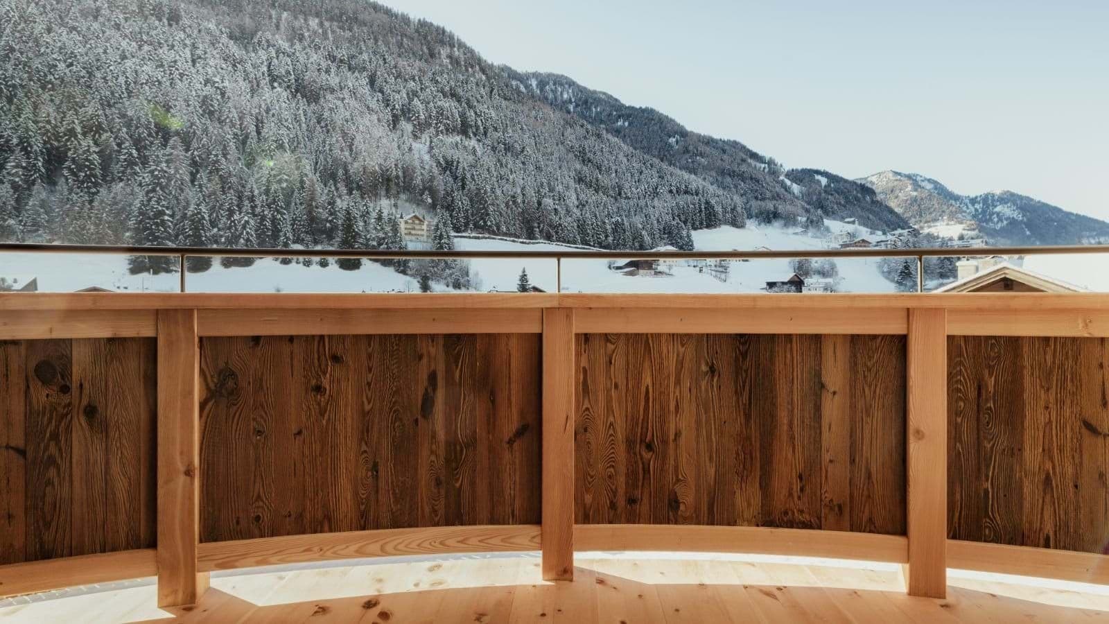 Deck with metal railing overlooks frozen lake and snow-covered mountains
