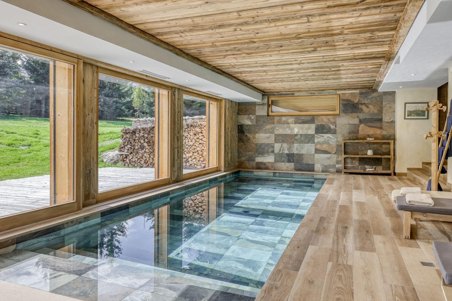Indoor heated pool with slate tile and floor-to-ceiling garden views