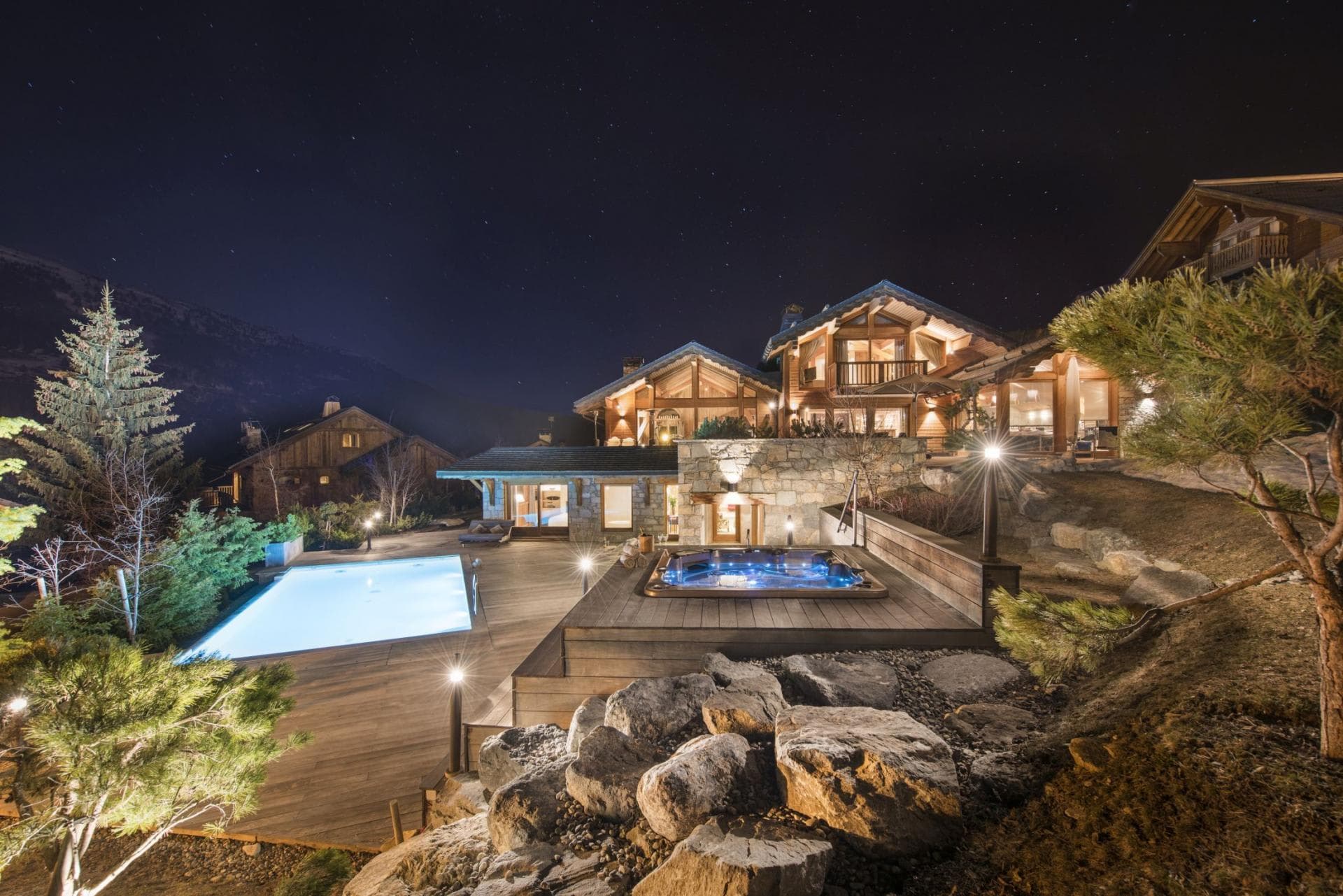 Illuminated outdoor pool and hot tub on timber decking at night