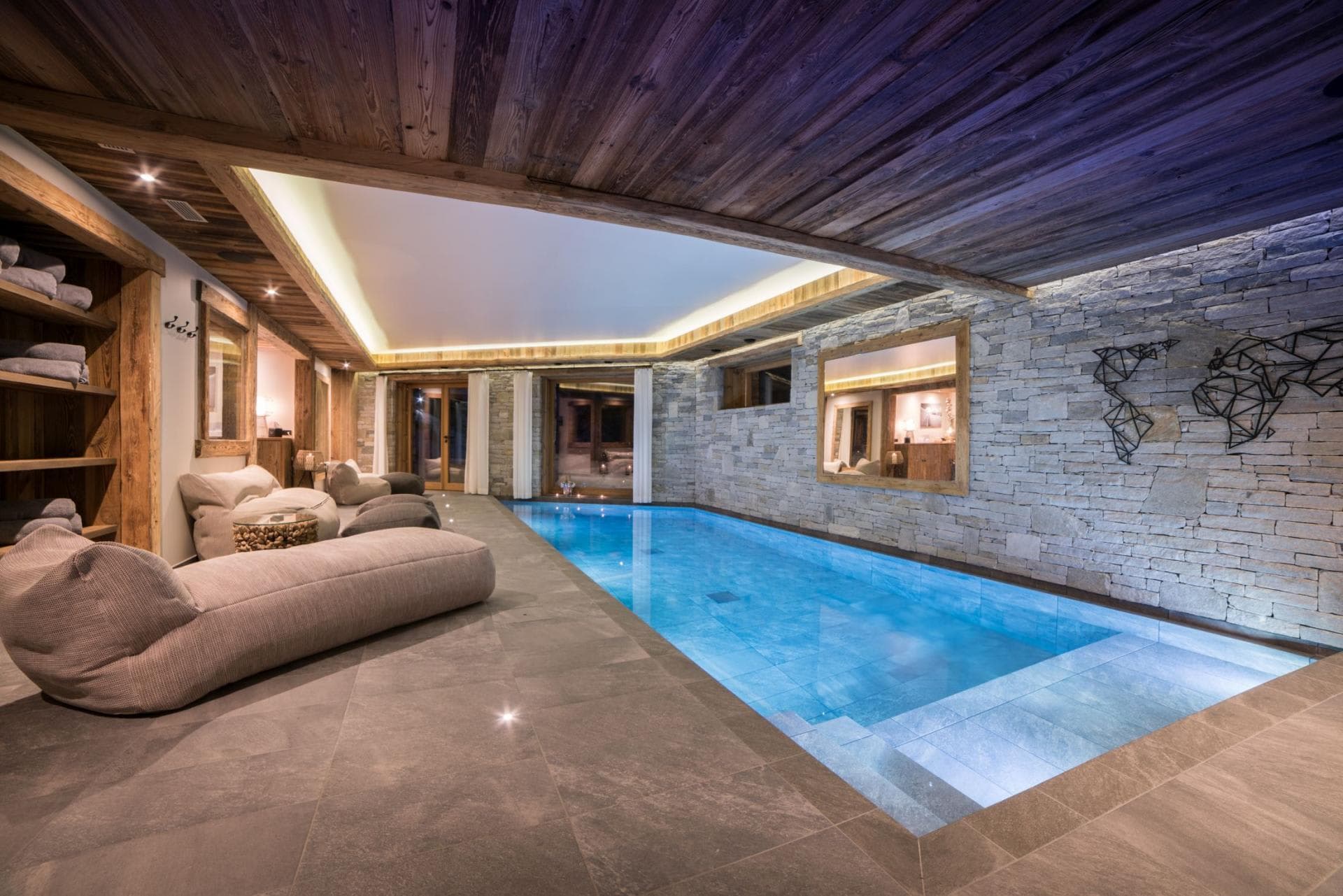 Indoor pool with stone wall, recessed lighting, and poolside lounge seating
