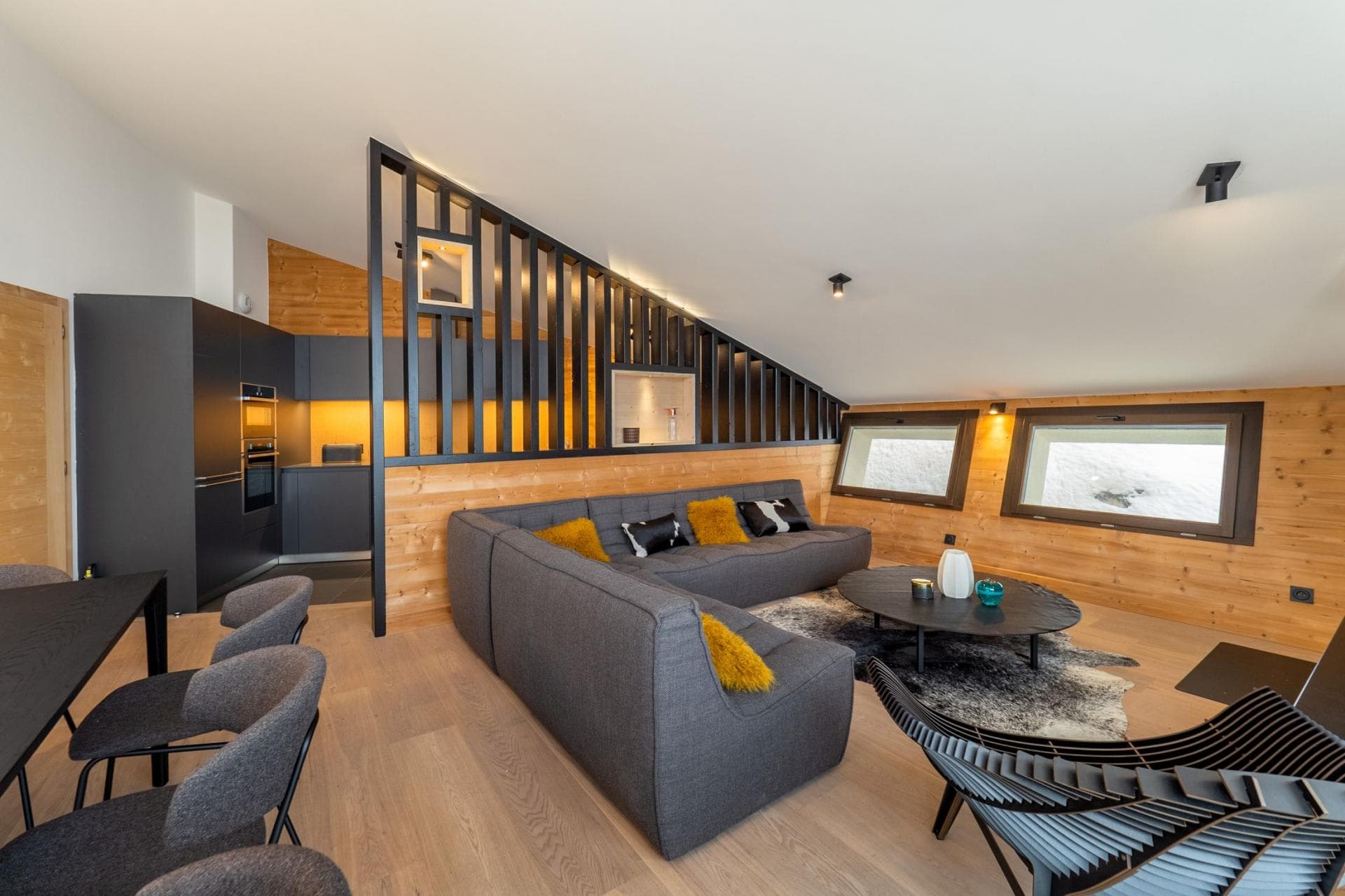 Open-plan living area with sectional seating and kitchenette behind slatted partition