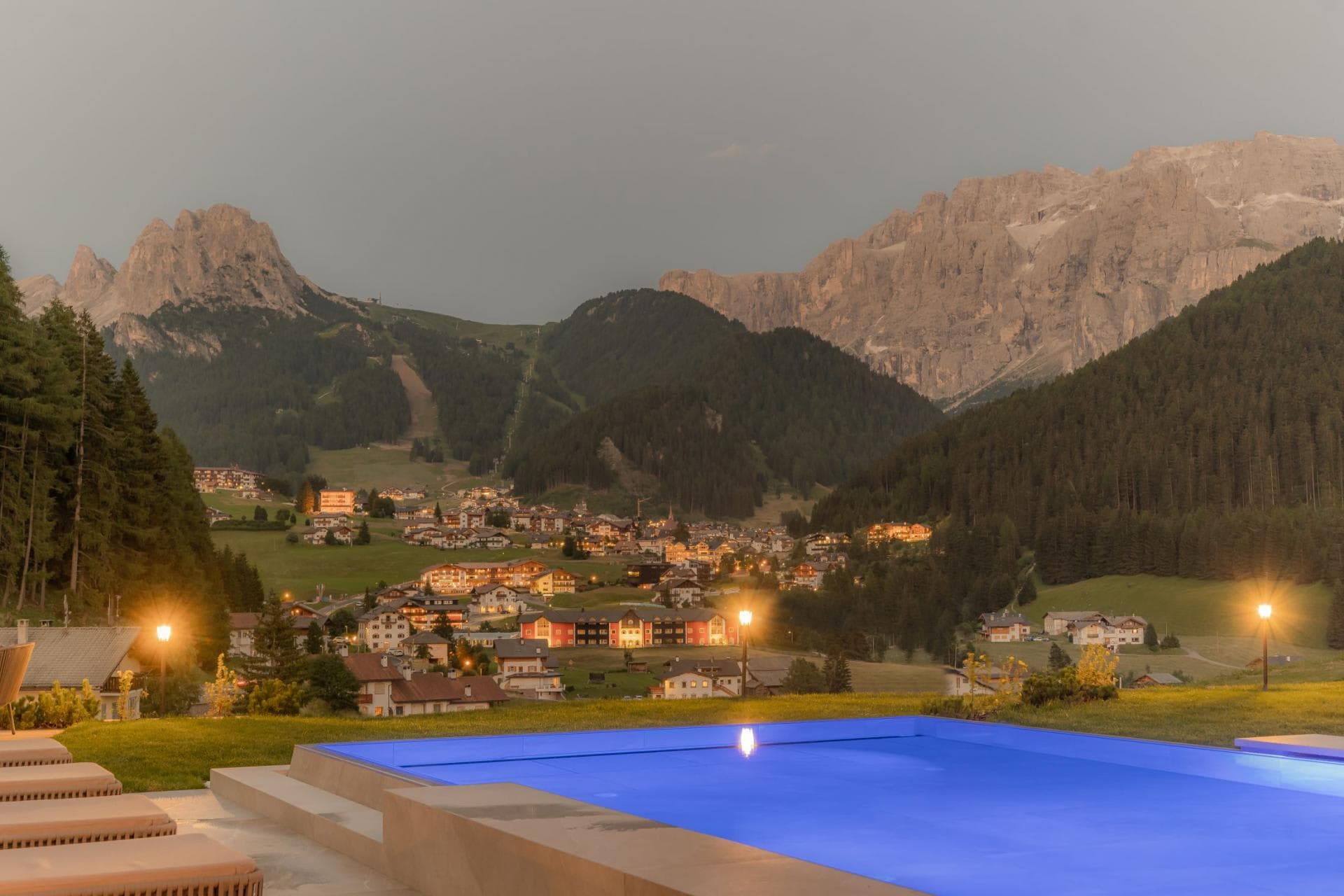 Illuminated infinity pool with views of Dolomite mountains and village