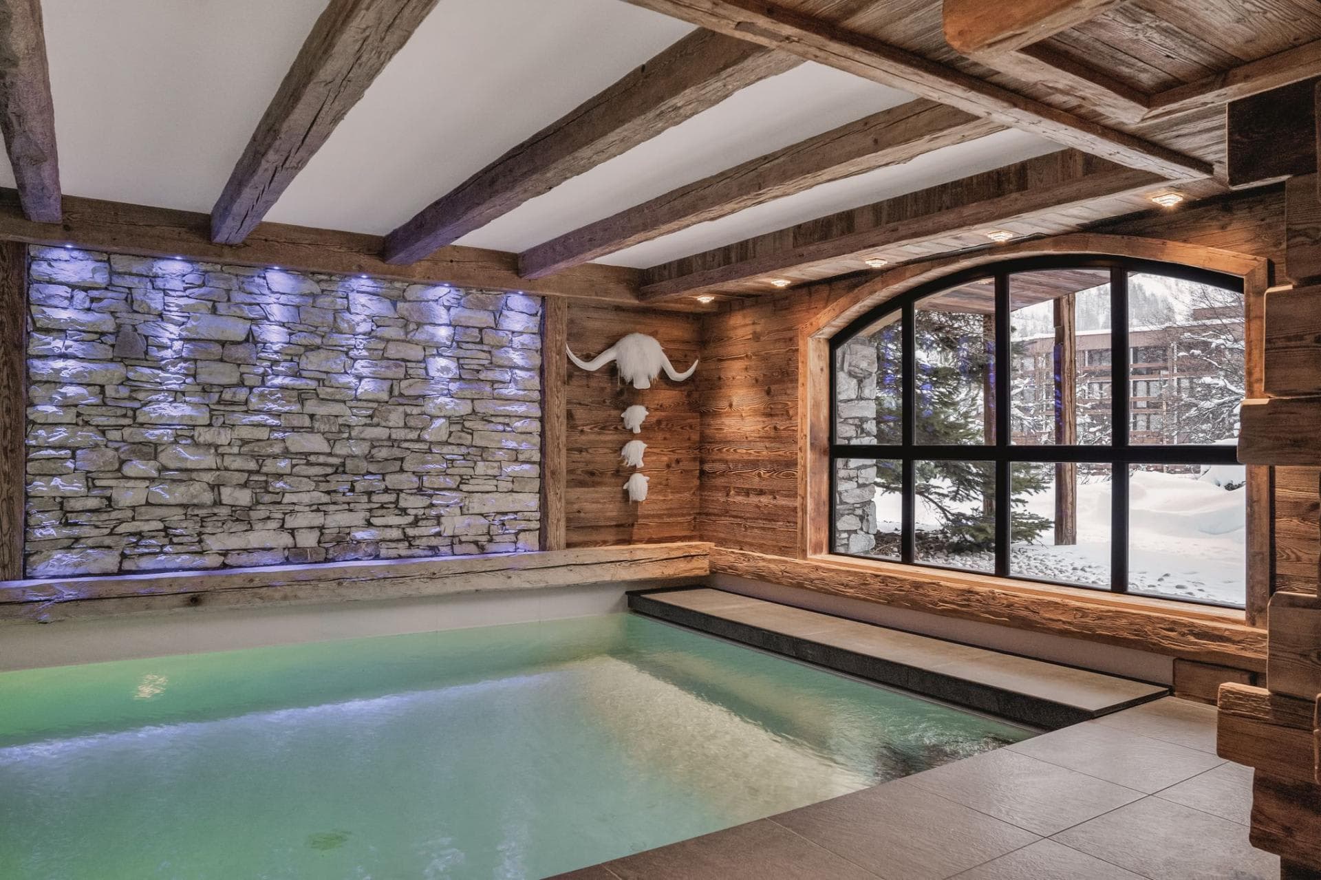 Indoor heated pool with stone feature wall and snowy forest views