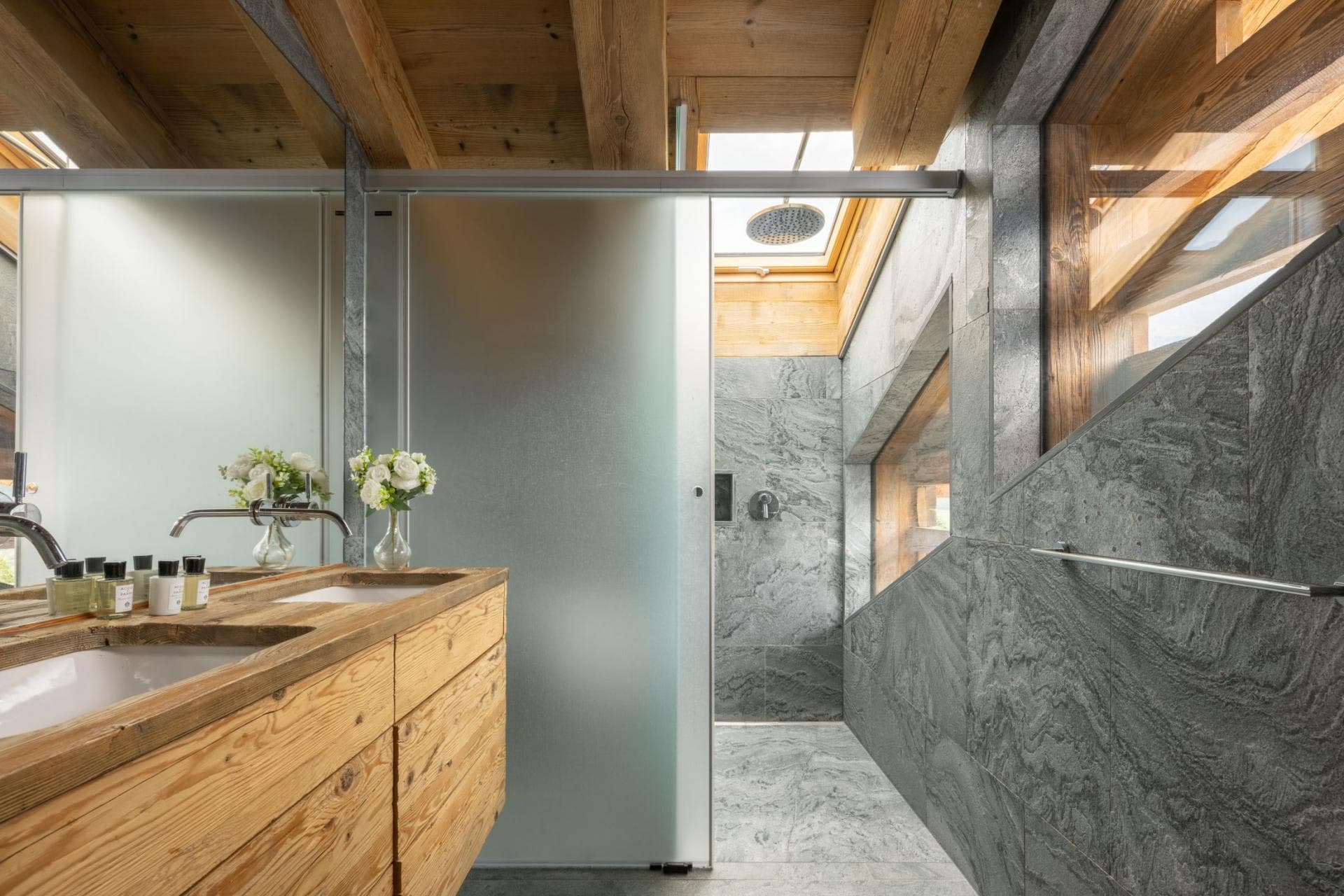 Bathroom with dual vanity and stone walk-in shower featuring overhead skylight