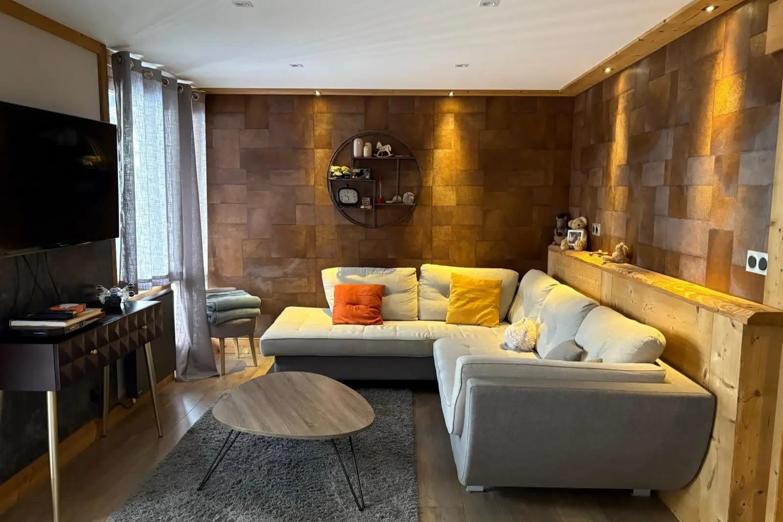 Living area with corner sectional, wall-mounted TV, and textured wood paneling