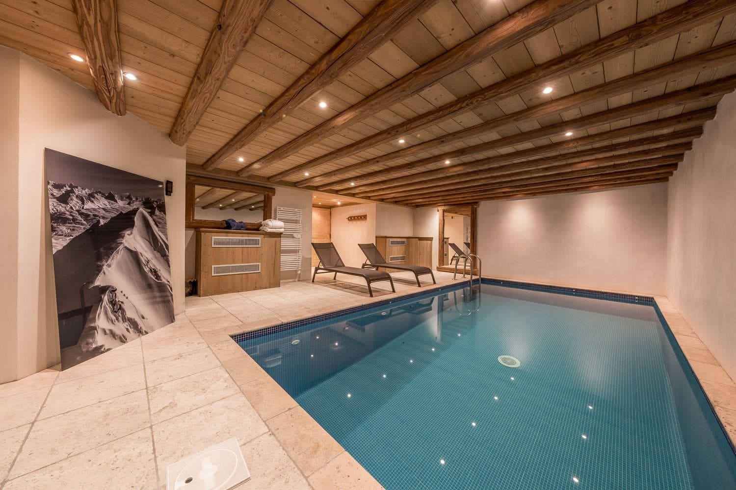 Indoor heated pool with poolside loungers and exposed timber ceiling