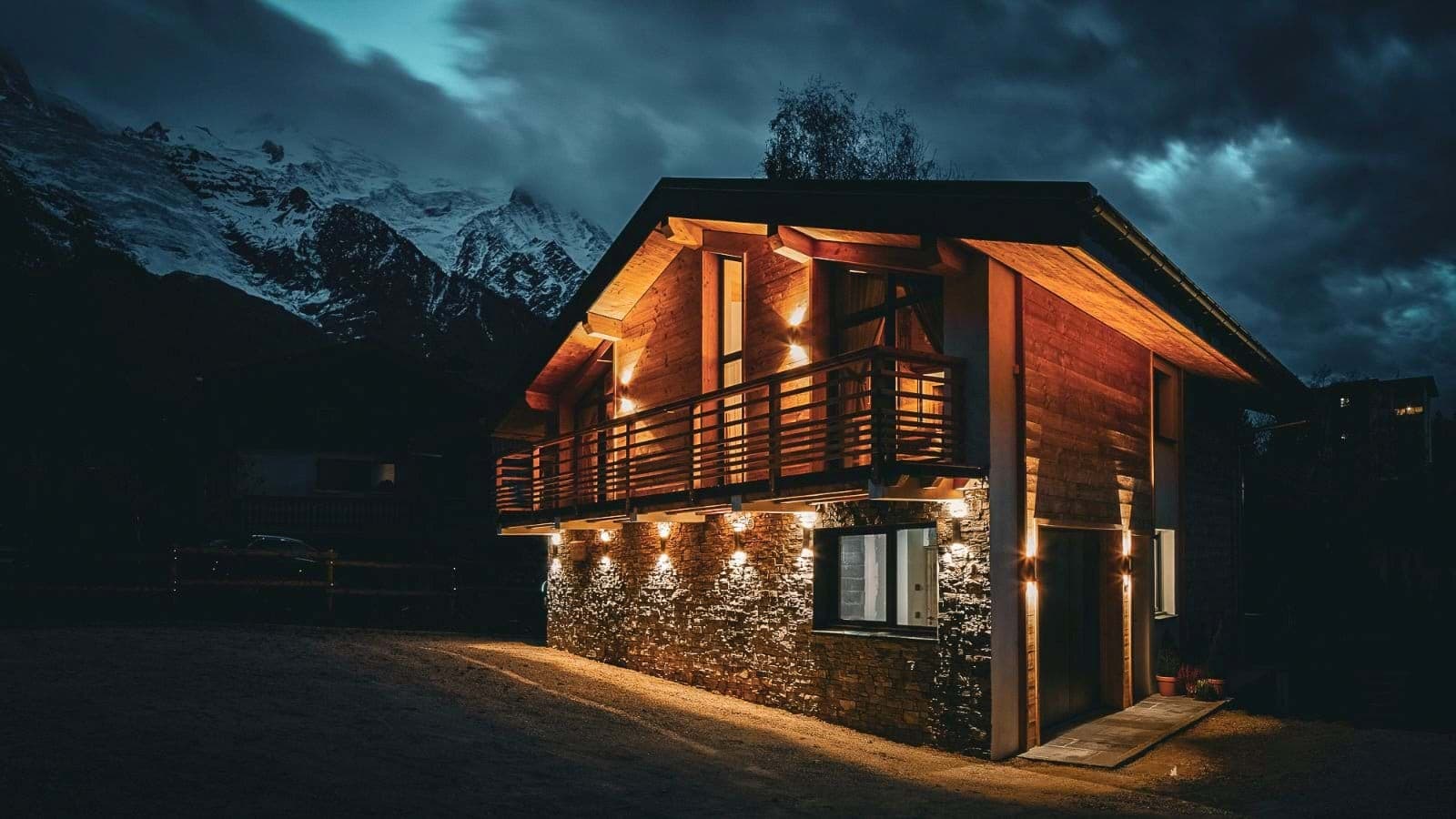 Chalet exterior with stone facade and upper-level balcony facing mountain peaks