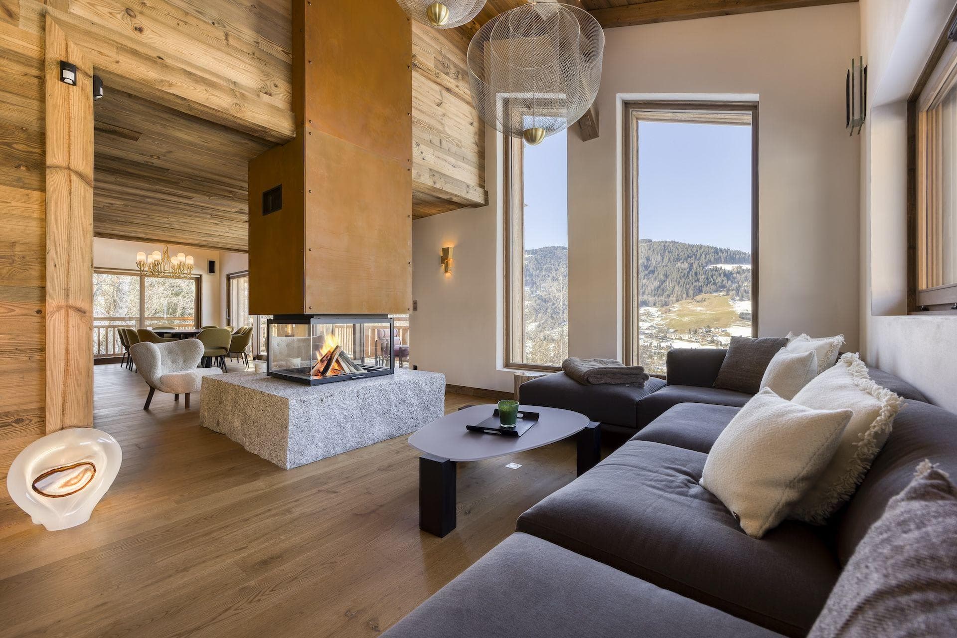 Living room with central glass fireplace and floor-to-ceiling mountain views