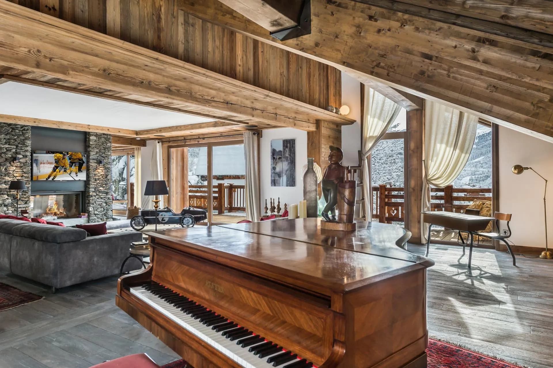 Living room with a grand piano, stone fireplace and mountain views