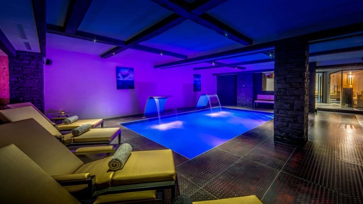 Indoor pool with waterfall features, lounge seating, and adjacent sauna