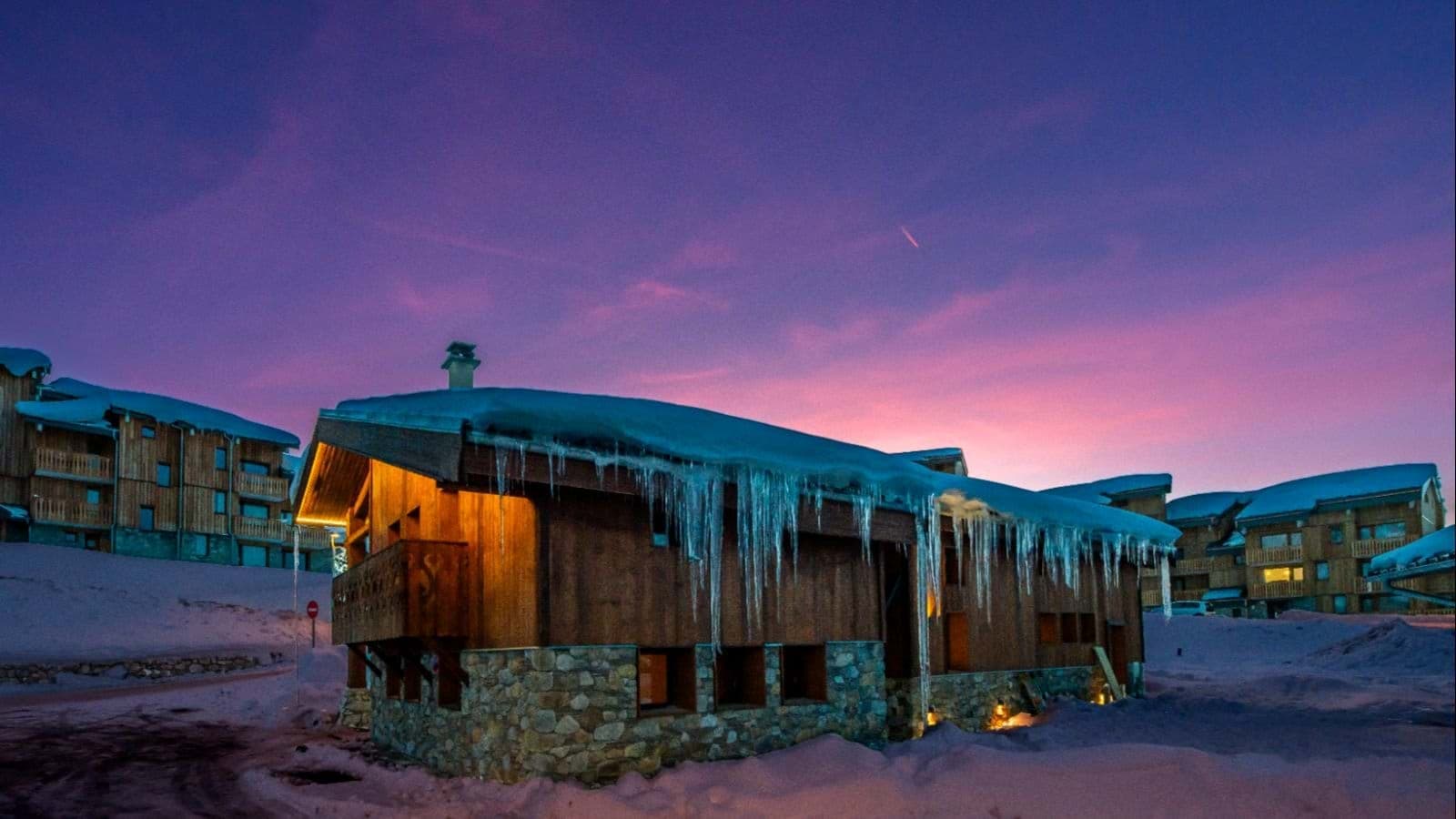 Ski-in chalet exterior with stone foundation and sunset mountain views