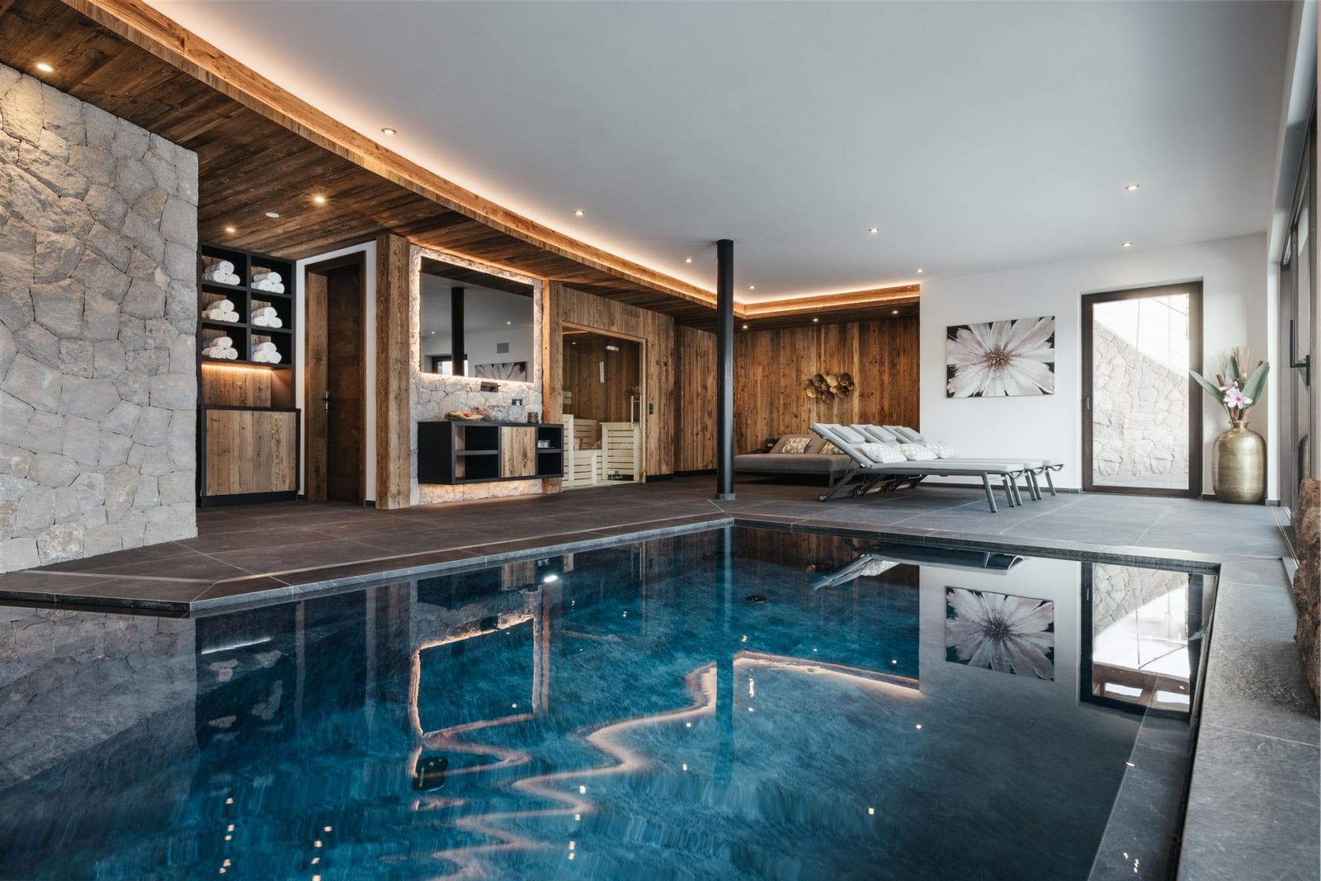 Indoor heated pool with adjacent sauna and poolside lounge chairs