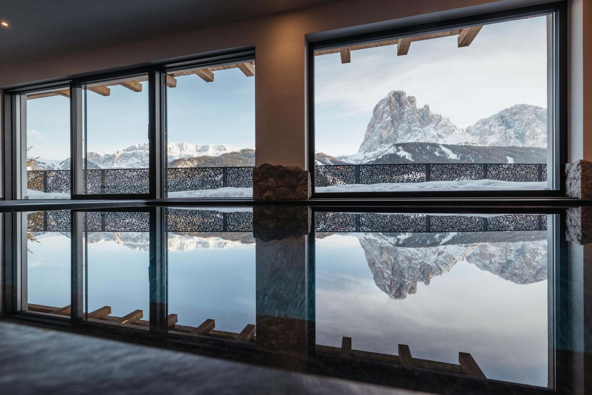 Indoor infinity pool with floor-to-ceiling windows and mountain peak views