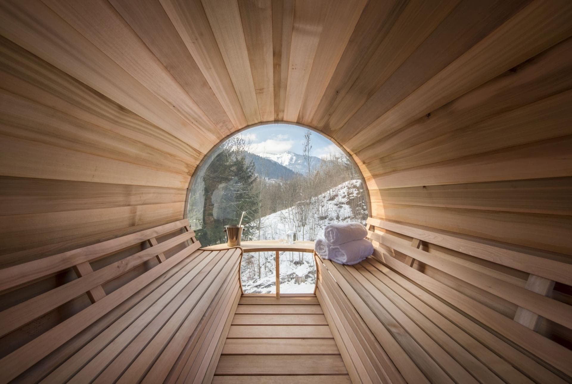 Barrel sauna with circular panoramic window and mountain views