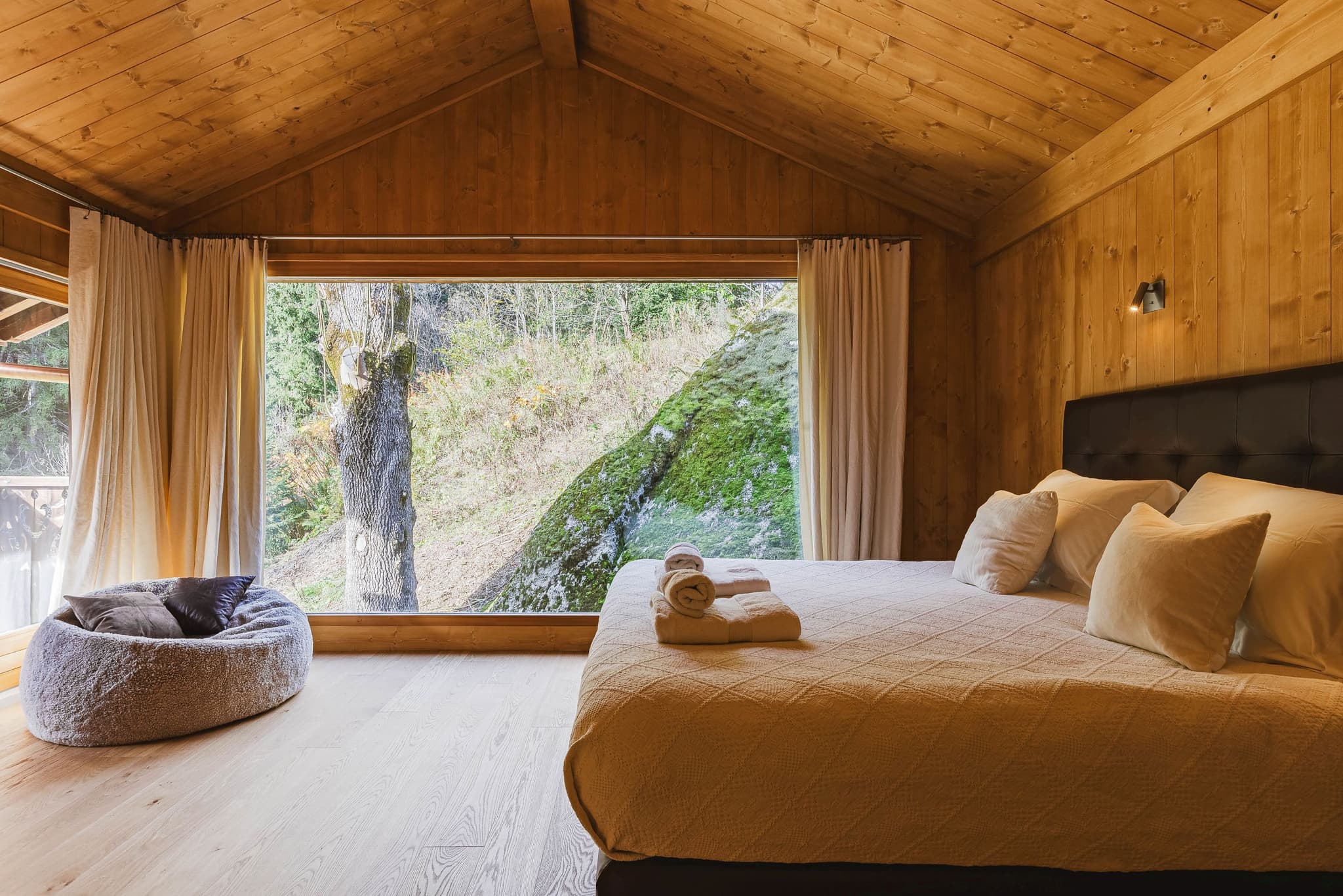 Wood-paneled bedroom with king bed and floor-to-ceiling forest views