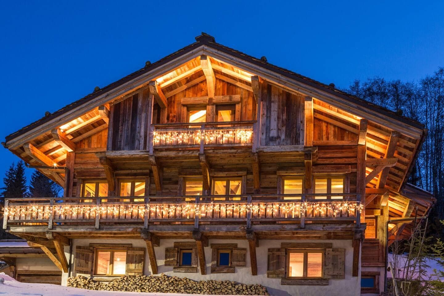Timber chalet exterior with multi-level lit balconies and firewood storage