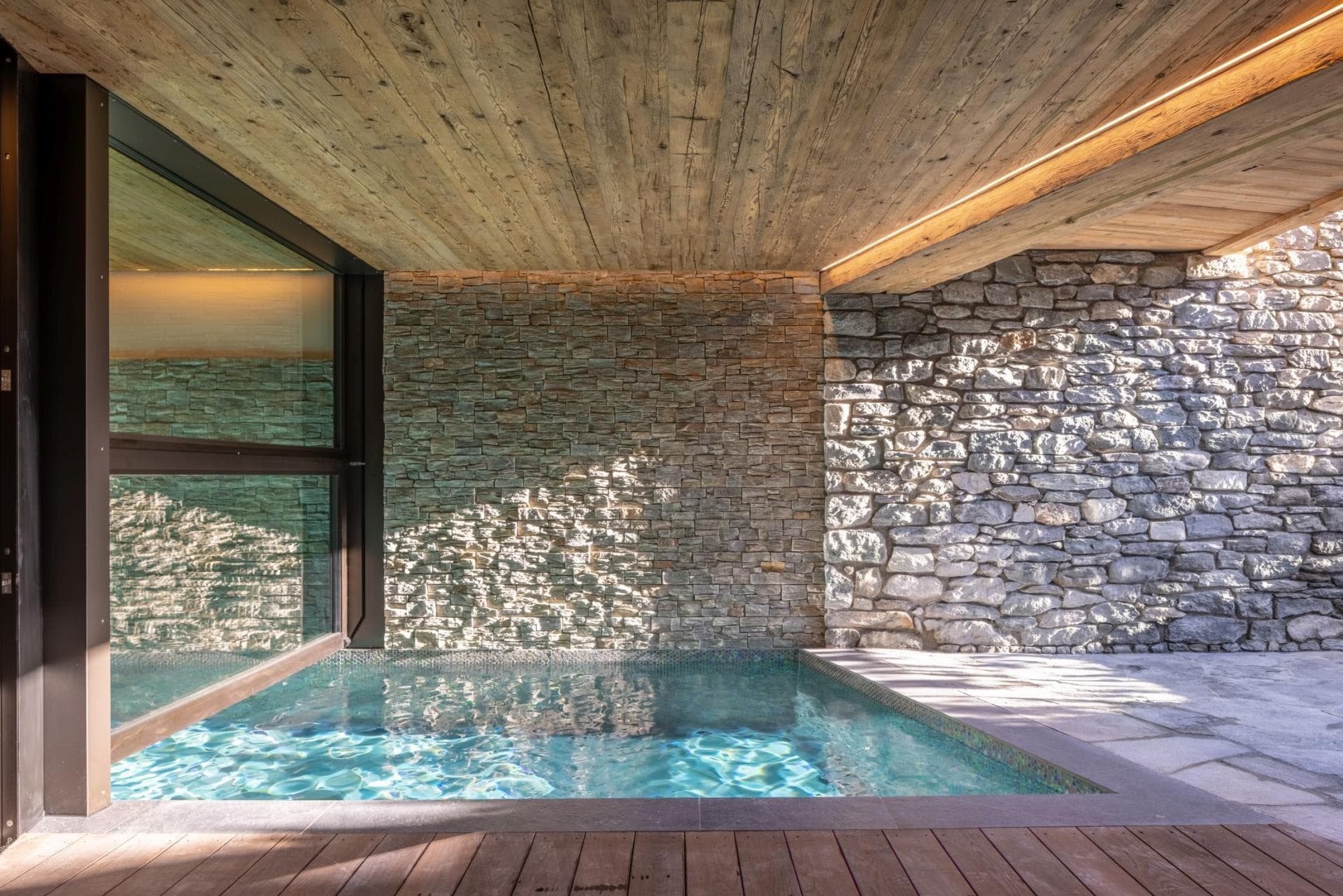 Indoor-outdoor plunge pool with stone walls and timber ceiling
