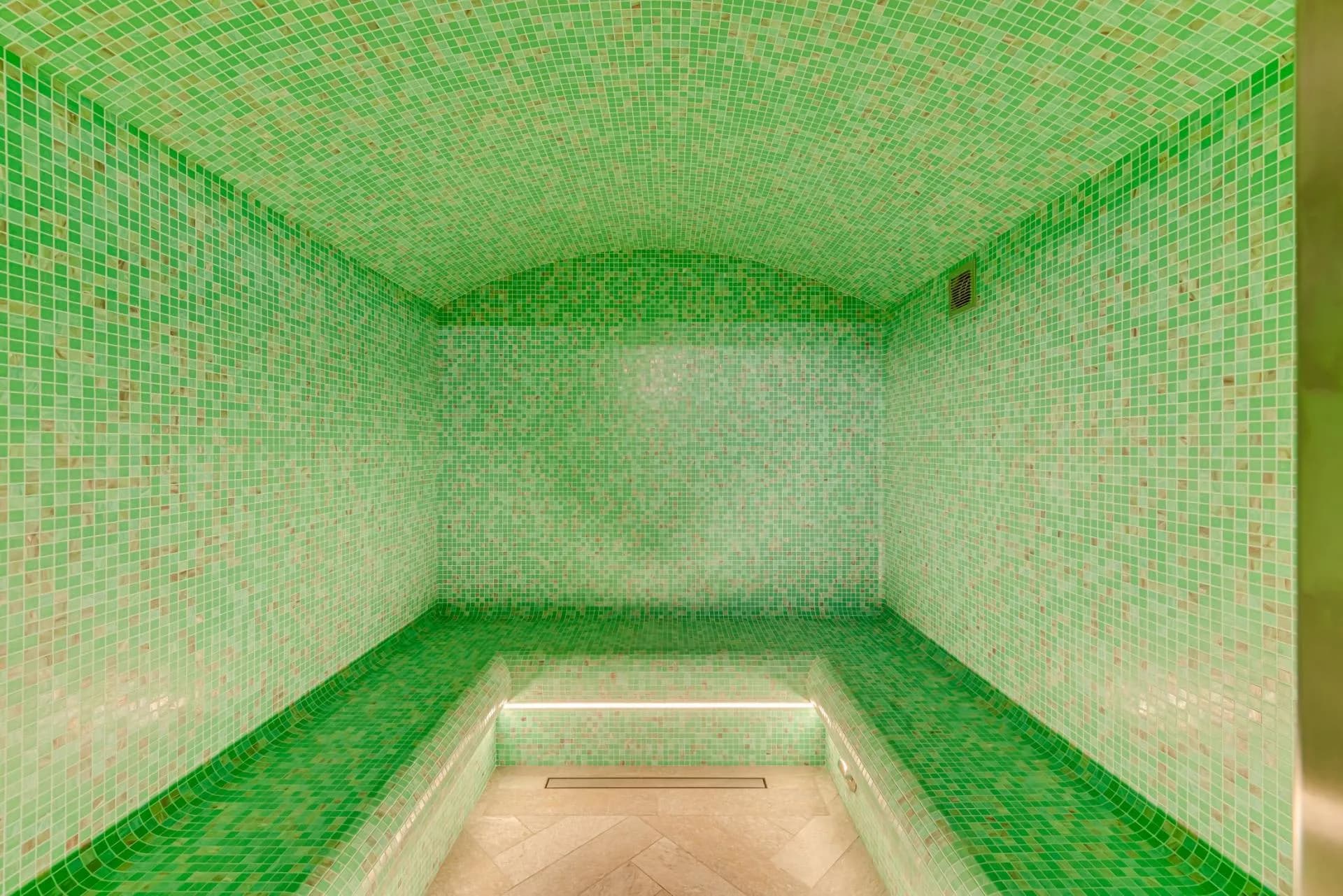 Private steam room with green mosaic tiles and built-in bench seating