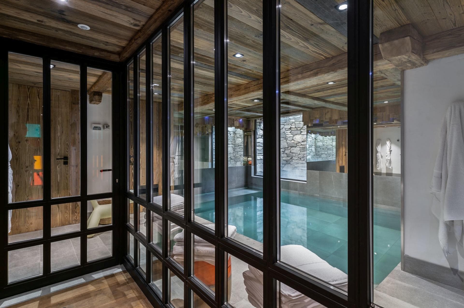 Indoor swimming pool viewed through glass partition with wood-beamed ceiling