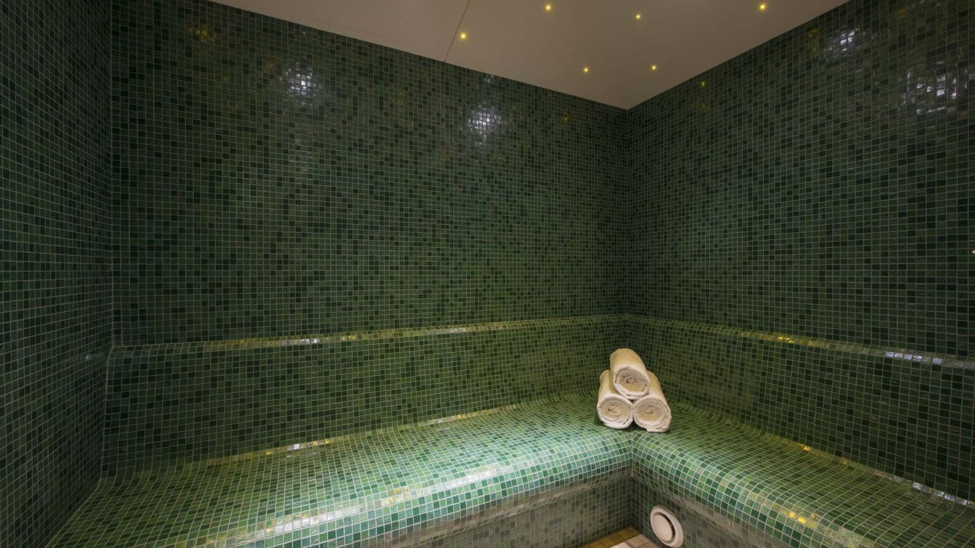 Private steam room with emerald mosaic tile and integrated bench seating