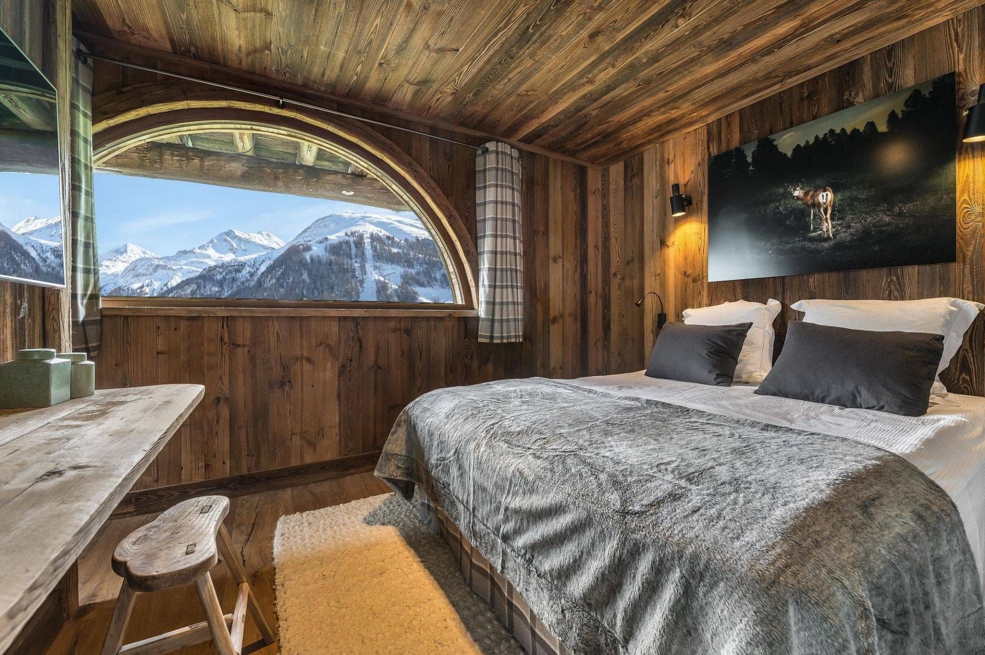 Wood-paneled bedroom with king bed, desk, and arched window mountain views