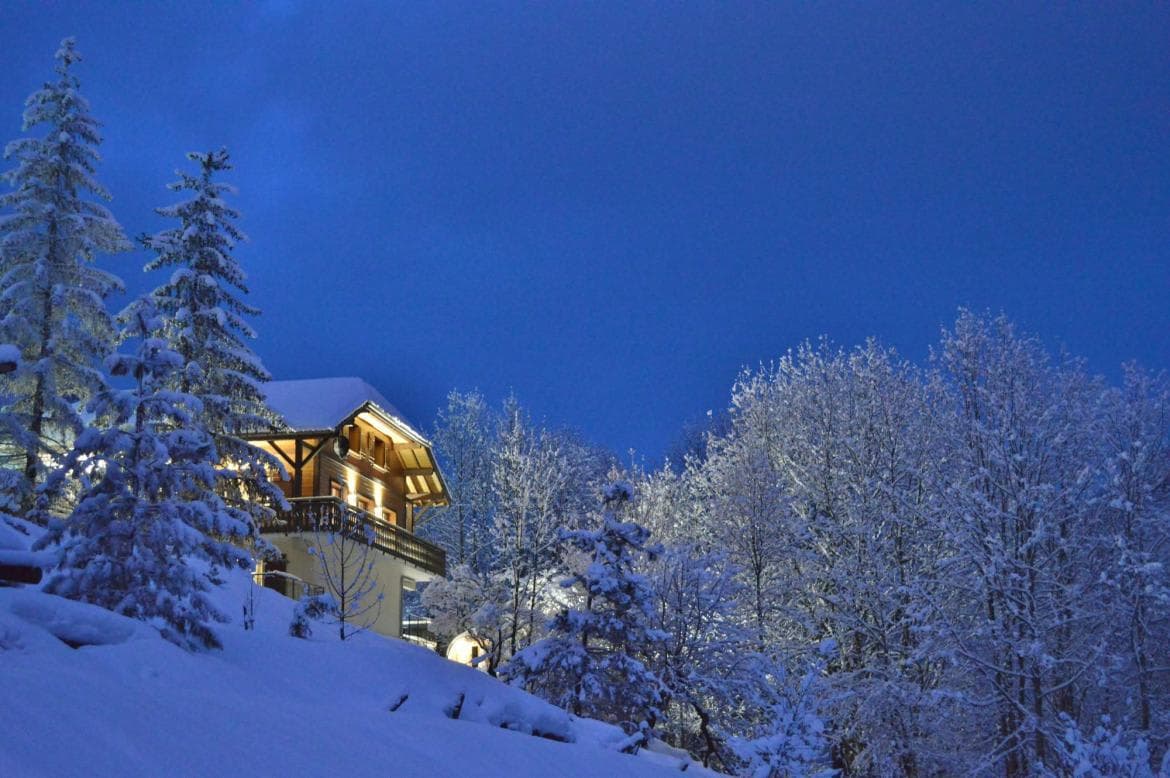 Chalet exterior at dusk with snow-covered trees and private balcony