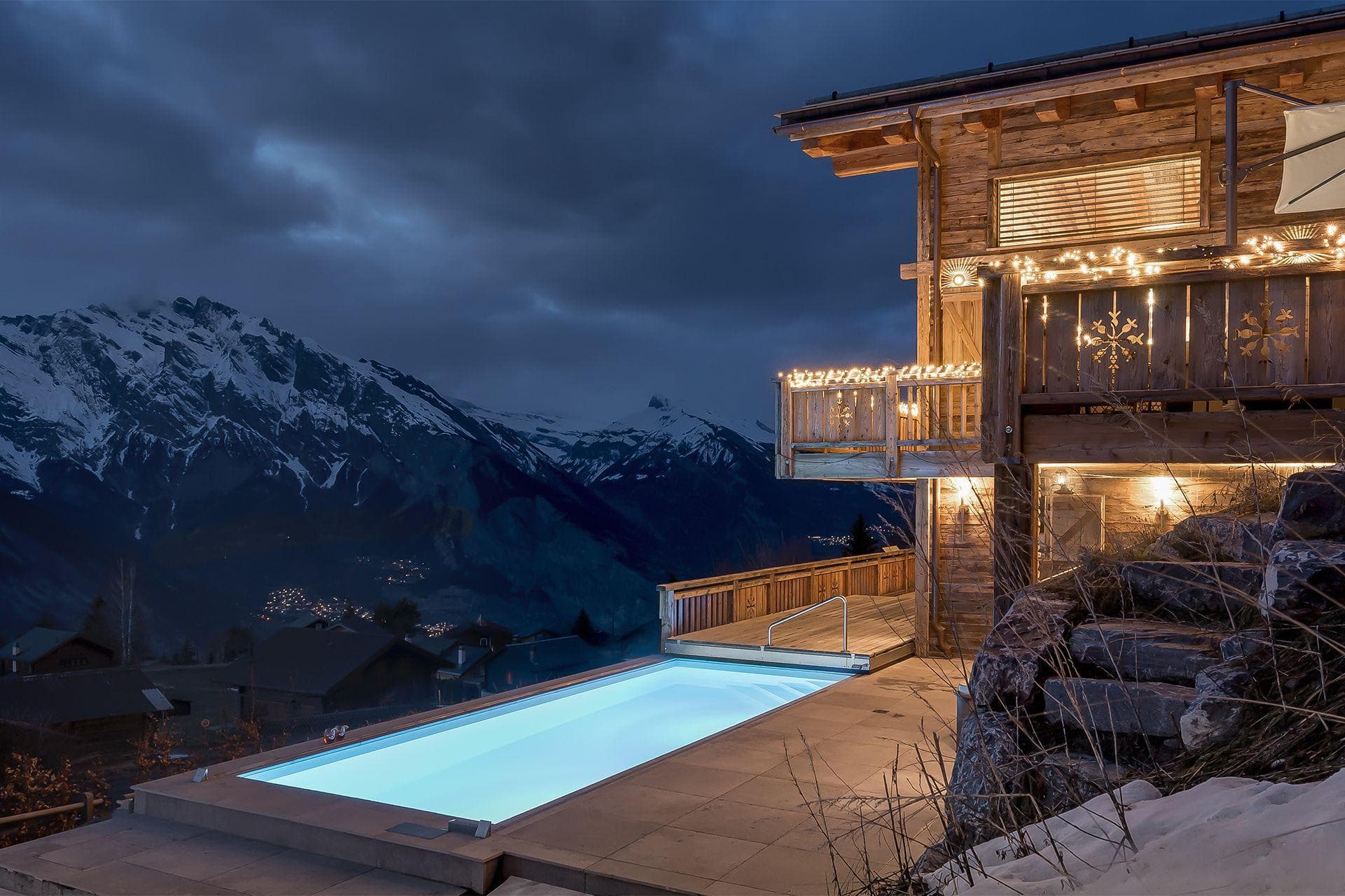 Outdoor pool with mountain views and illuminated chalet deck