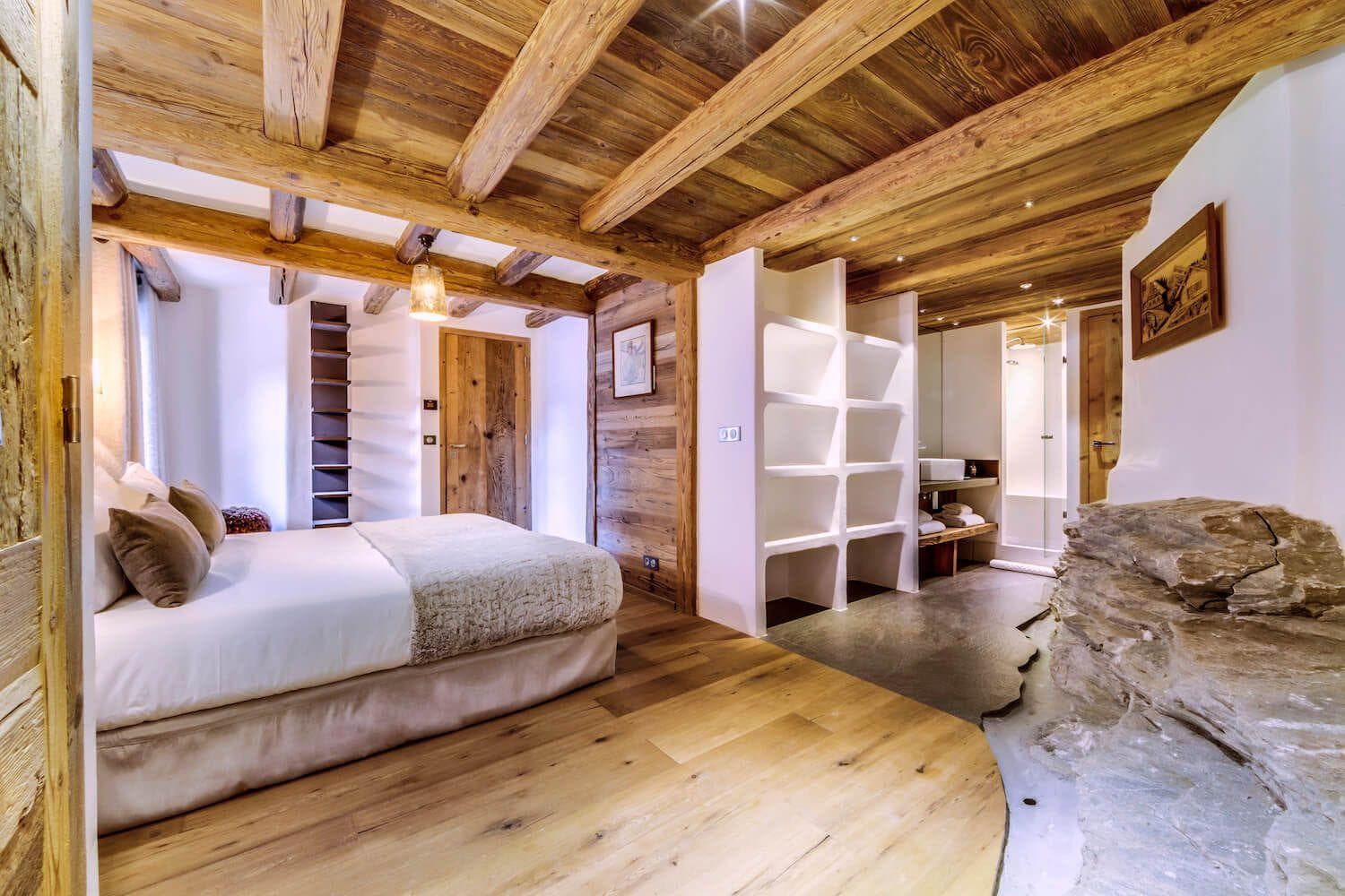 Primary bedroom with ensuite bathroom, exposed beams, and natural rock feature