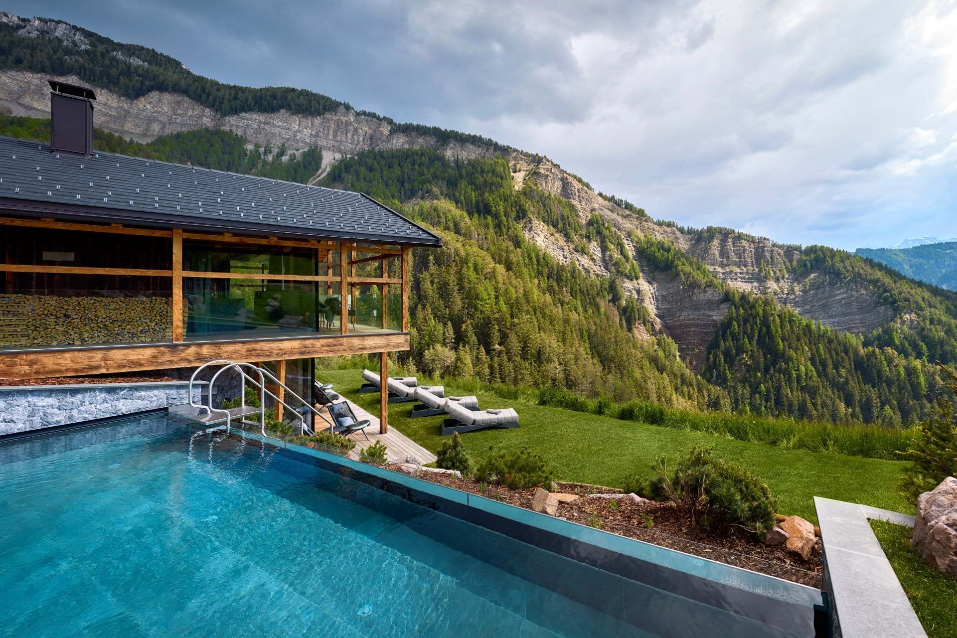 Glass-walled infinity pool and lawn with mountain cliff views