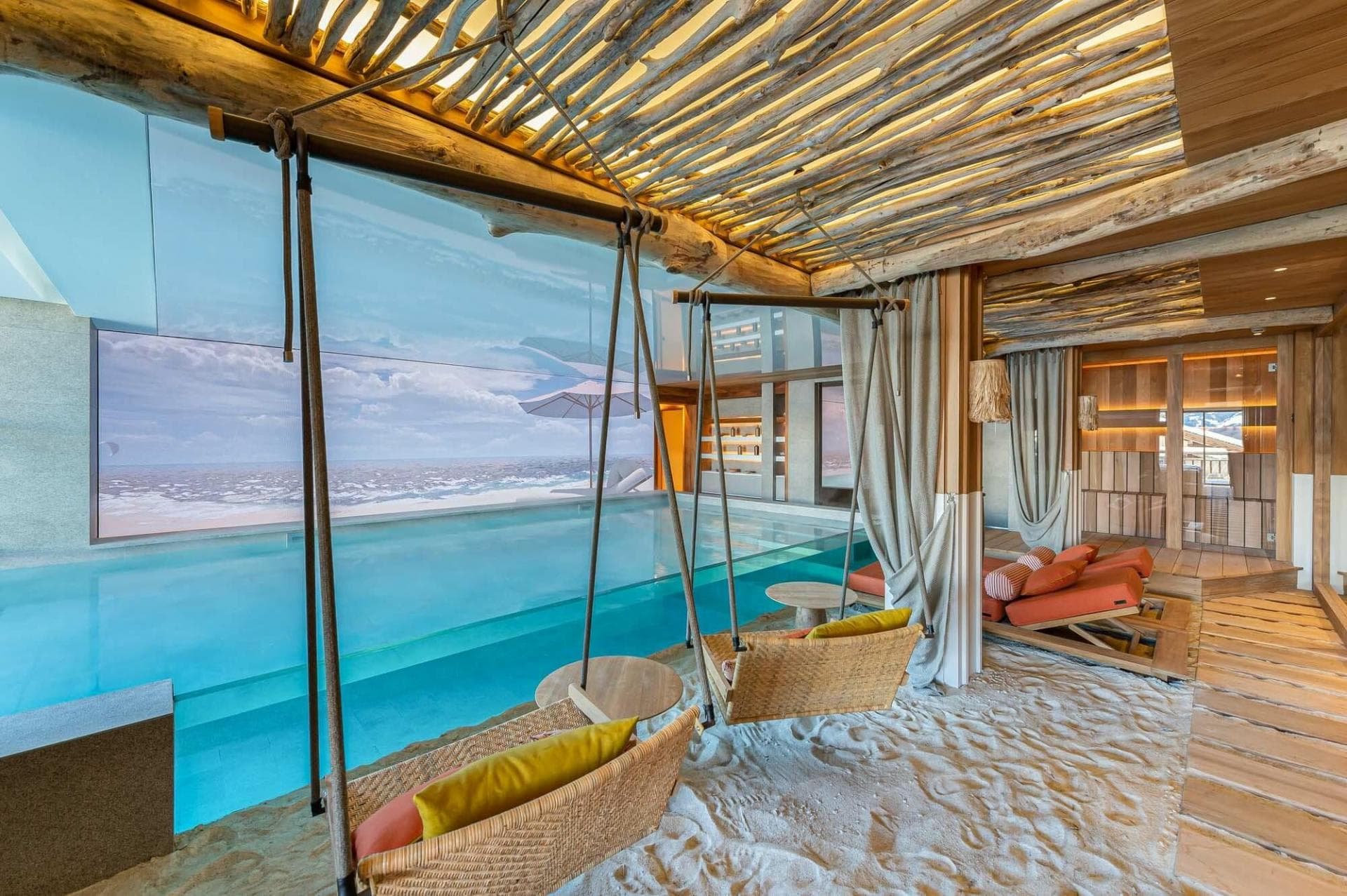 White-sand lounge with hanging swings beside the indoor swimming pool