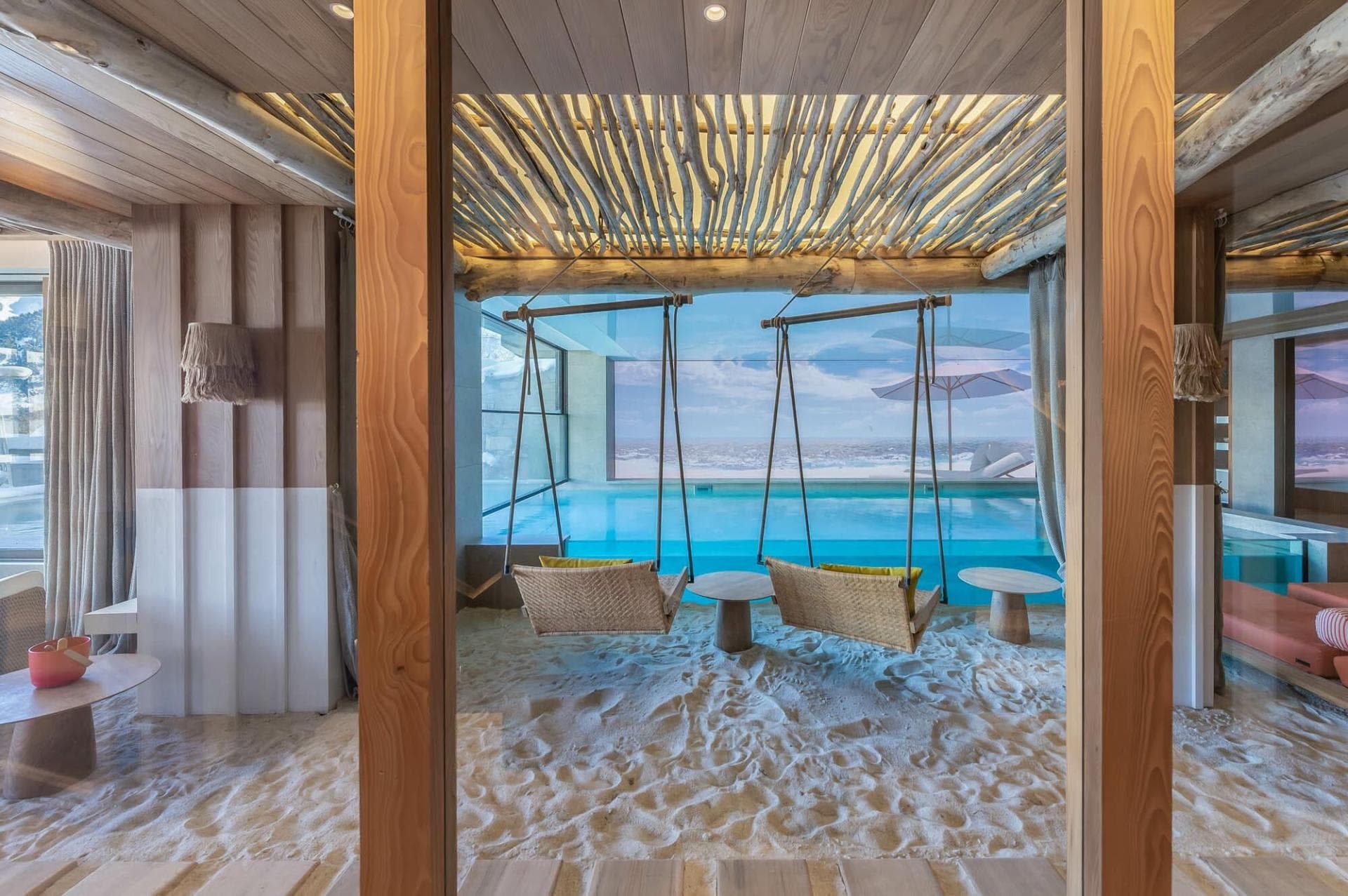 Indoor lounge with real sand floor and swings overlooking infinity pool