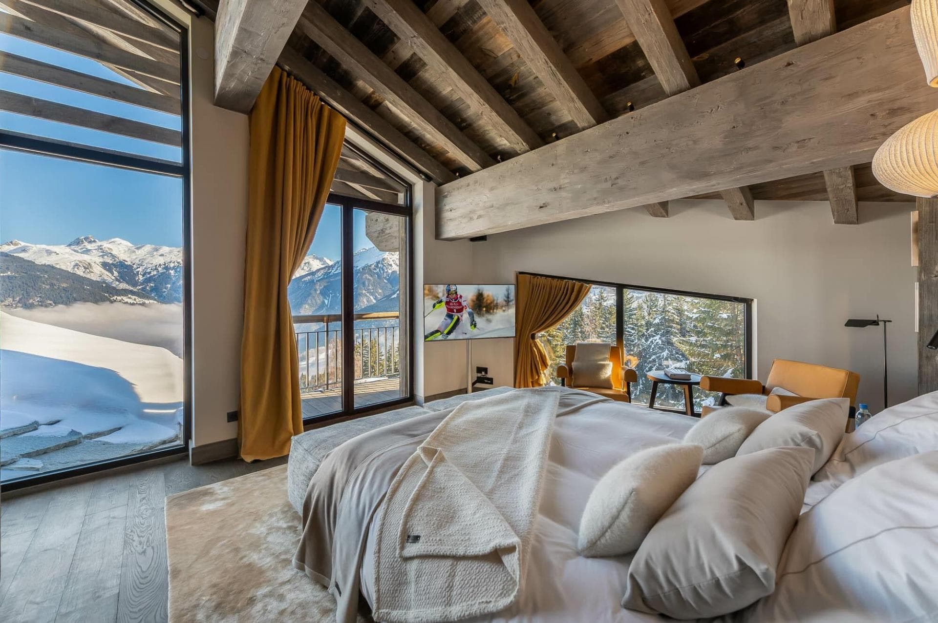 Primary bedroom with private balcony, mountain views, and vaulted timber ceilings