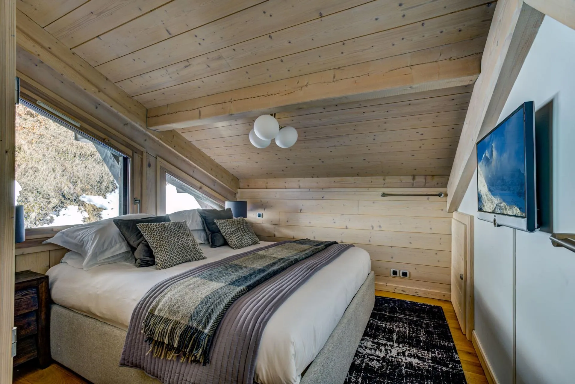 King bedroom with wall-mounted TV and slanted wood-paneled ceiling