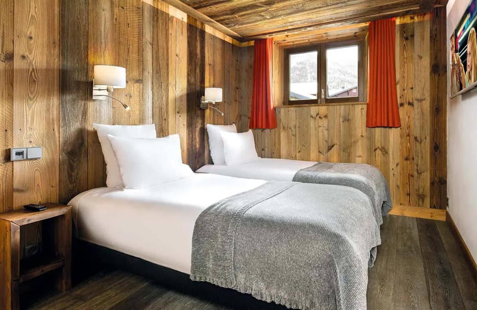 Twin bedroom with rustic wood walls and wall-mounted reading lamps