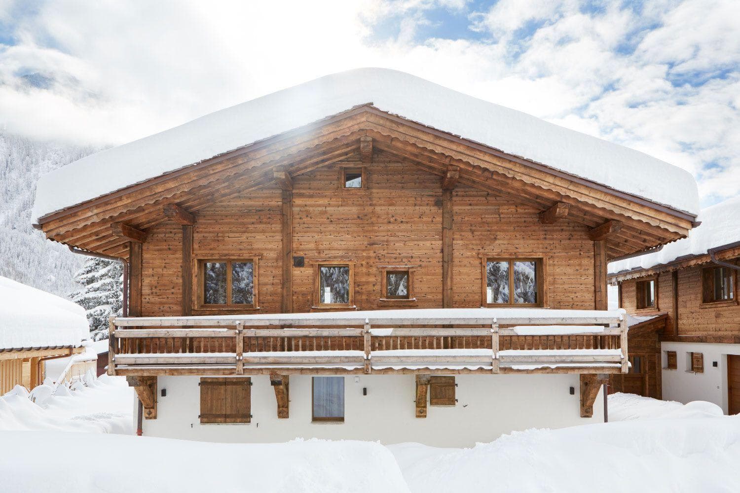 Three-level timber chalet with full-width balcony and snow-covered roof