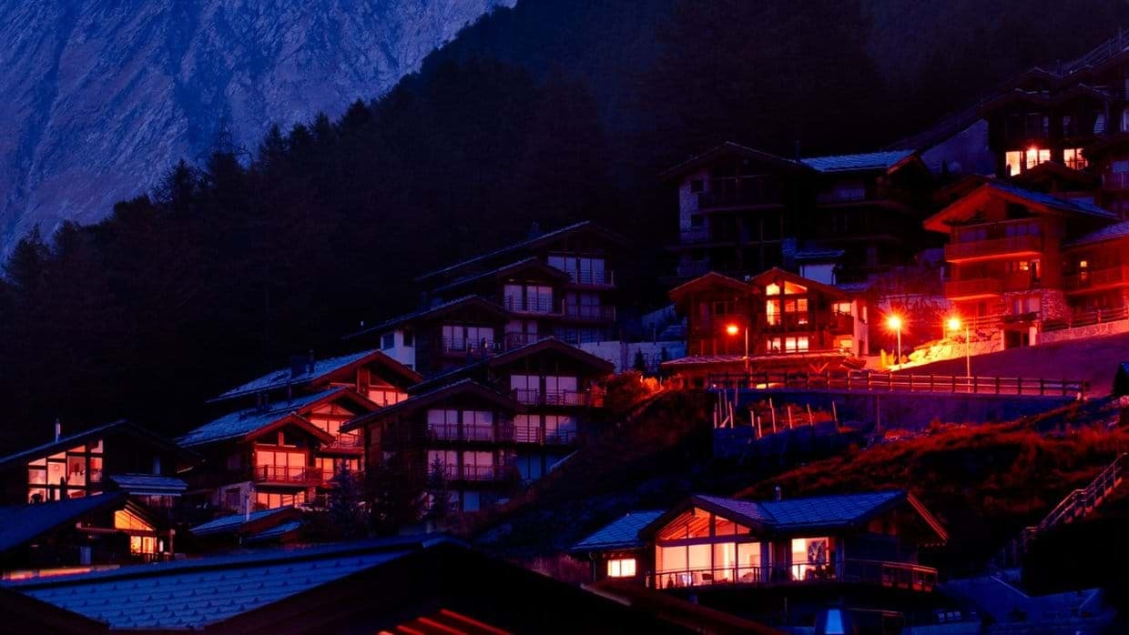 Illuminated hillside chalets at night with mountain backdrop