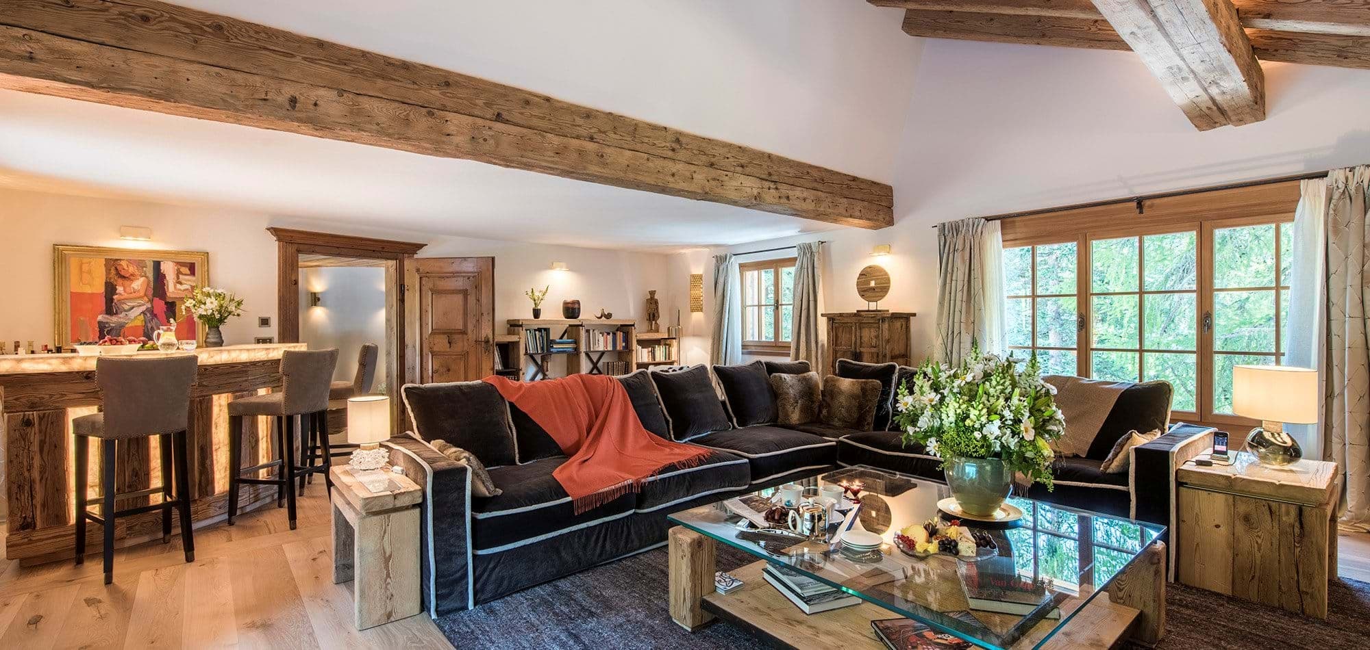 Living area with reclaimed wood beams, bar seating, and forest views