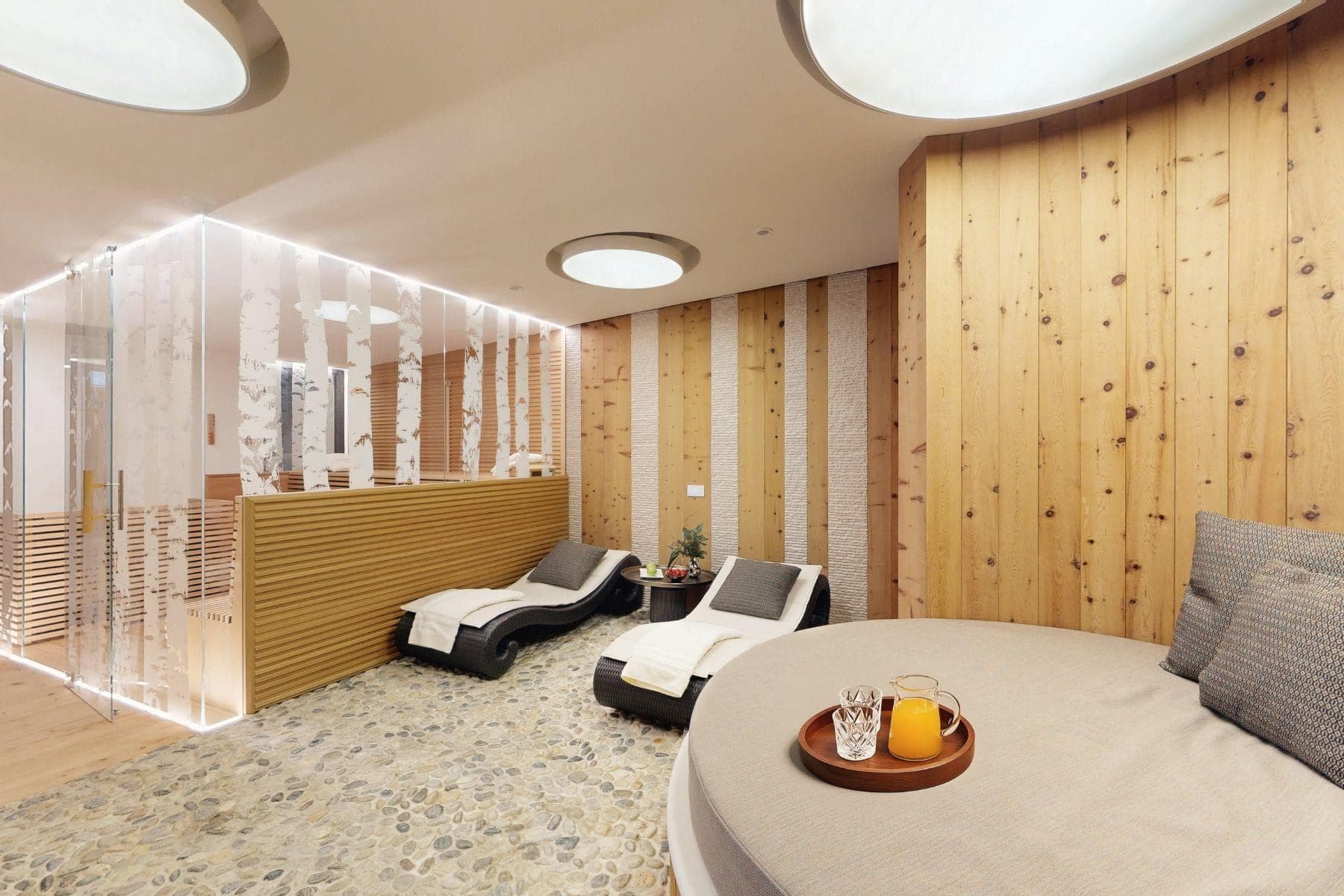 Spa lounge with heated pebble flooring, loungers, and glass-enclosed sauna